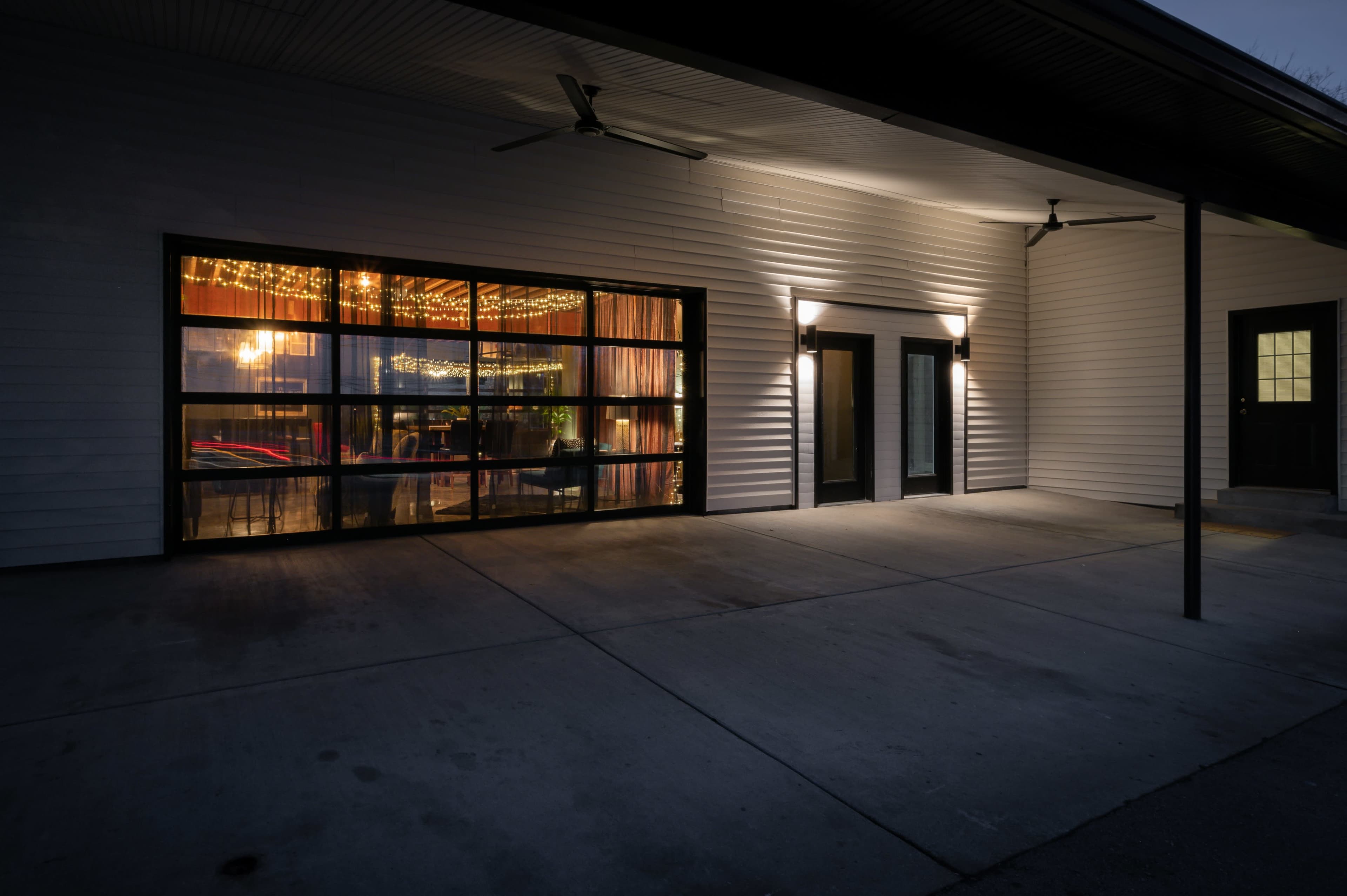 The image shows a dimly lit exterior of a building with large windows revealing an illuminated interior and two entrance doors on either side.