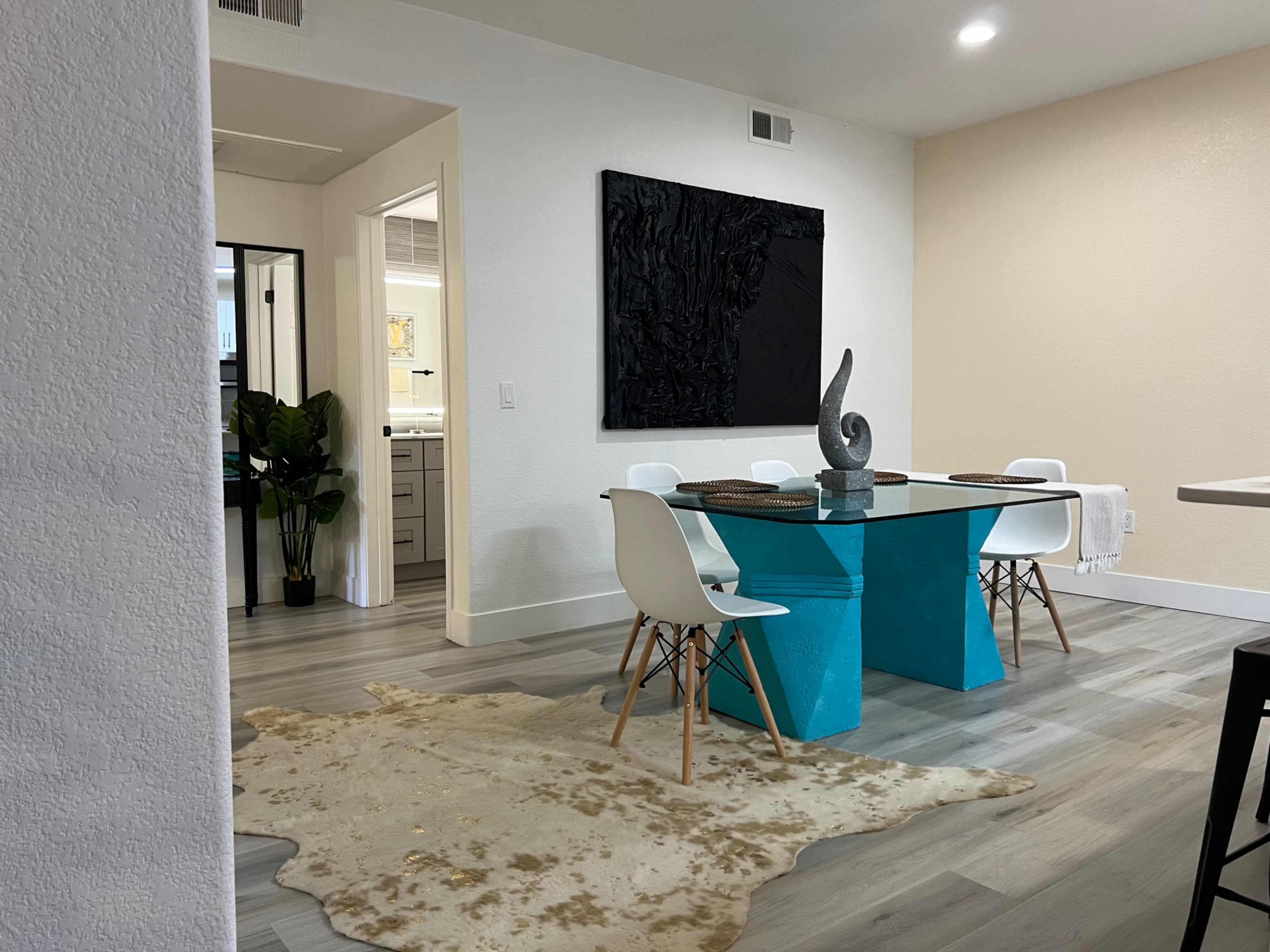 A dining area features a turquoise table surrounded by white chairs, with a decorative sculpture on top and a cowhide rug beneath.