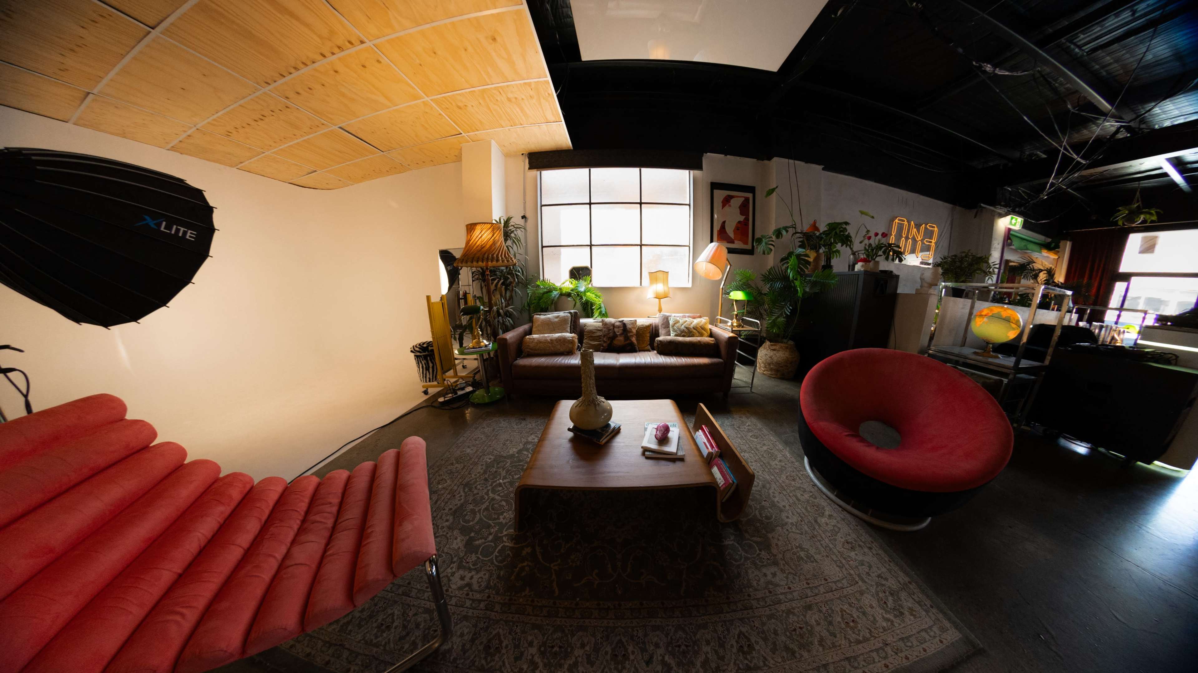 The image shows a cozy indoor space with various seating areas, a large green plant, and stylish lighting fixtures.