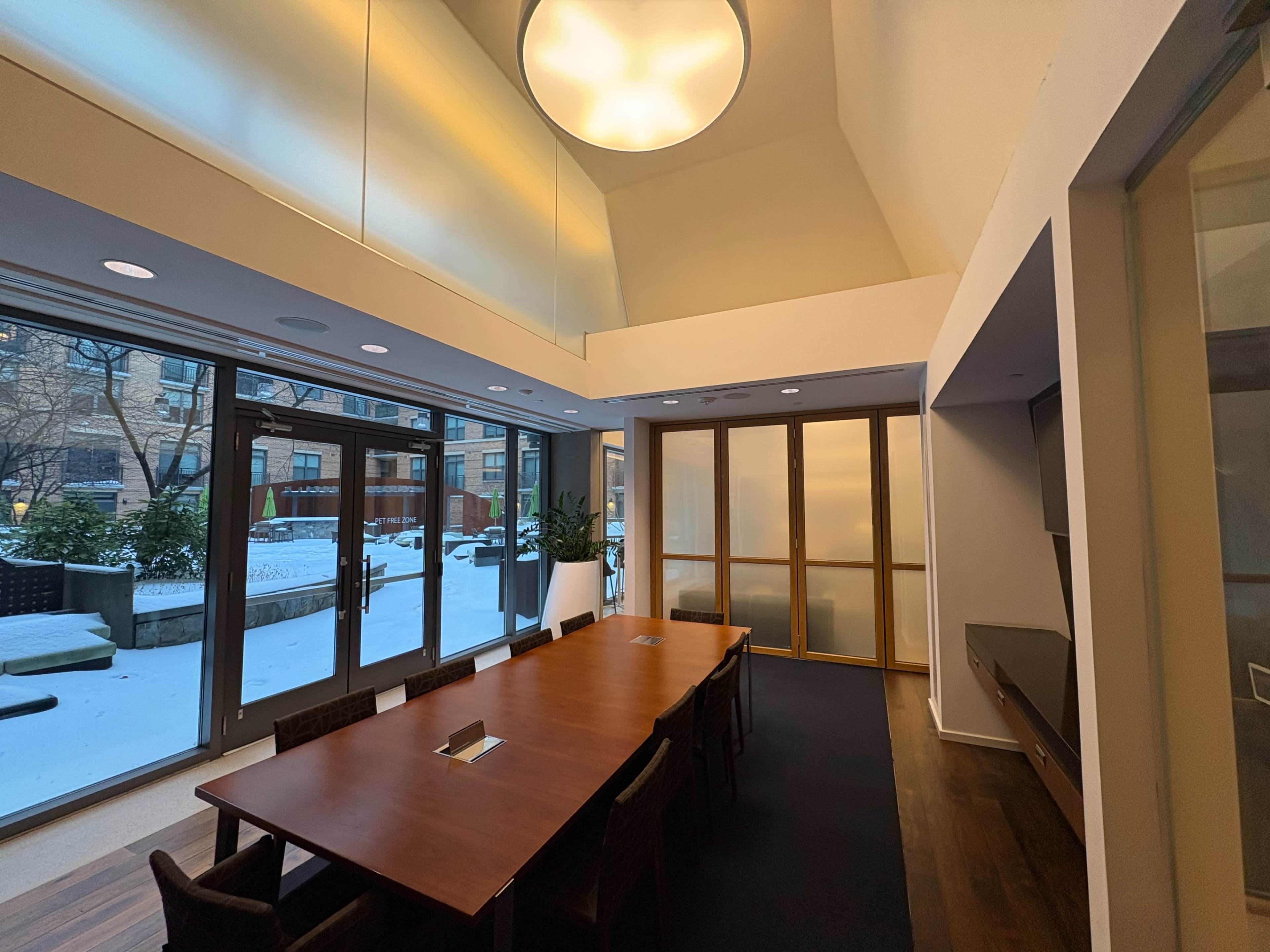 The image shows a modern conference room with a large wooden table, surrounded by chairs, and large windows displaying a snowy outdoor landscape.