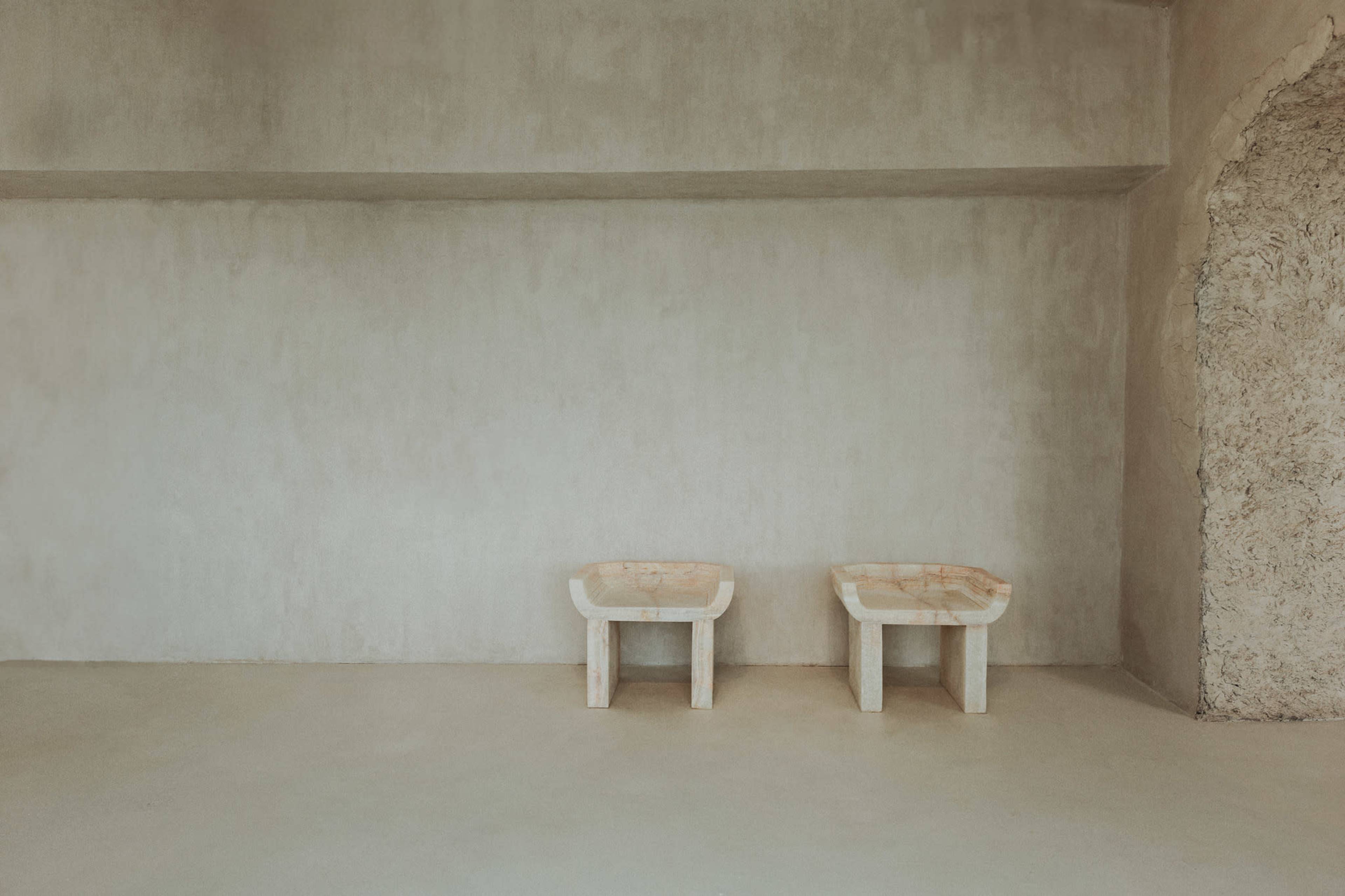 The image shows two minimalist stone sinks positioned on an unfinished concrete floor against a plain wall.