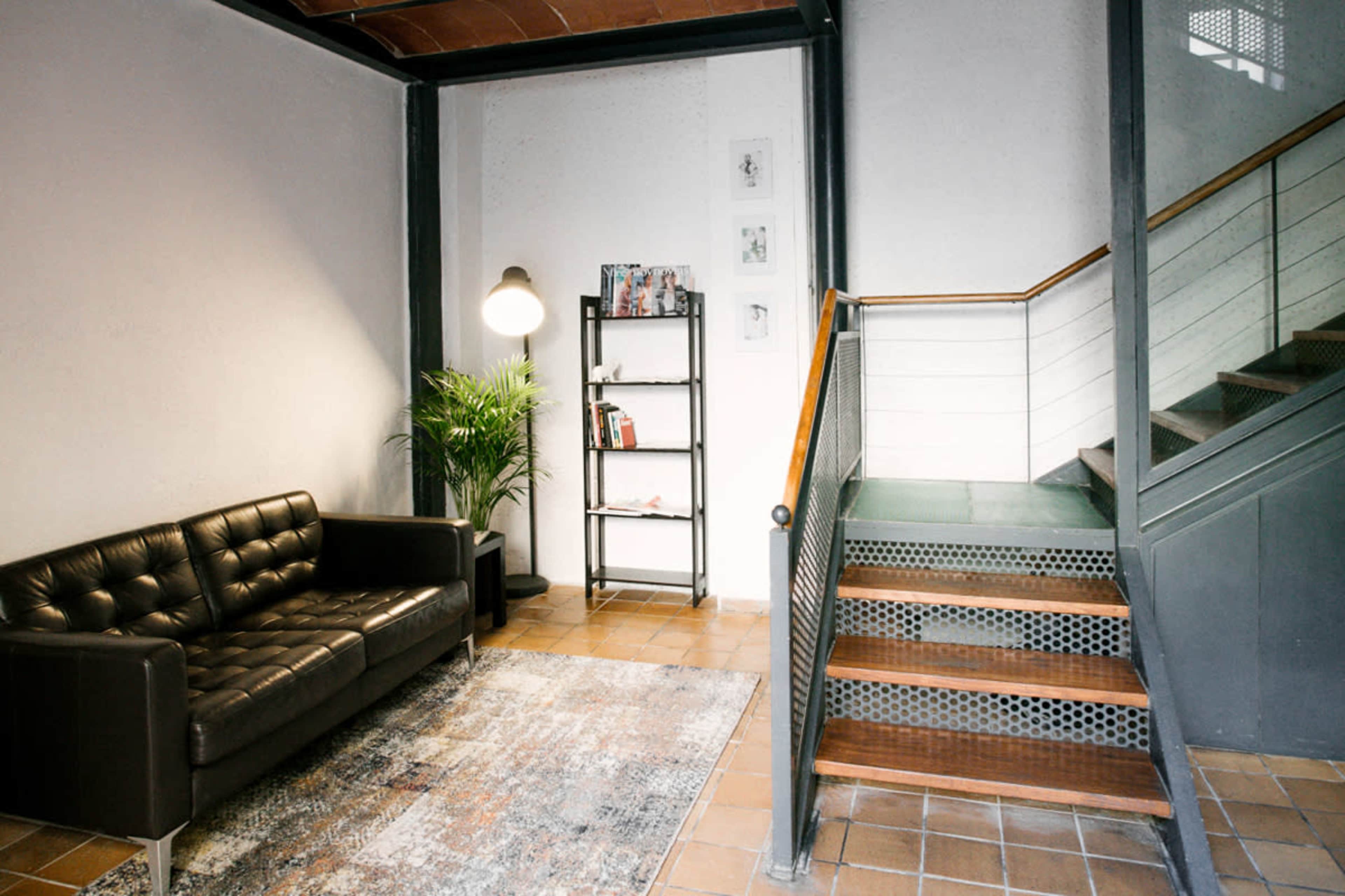 A modern stairwell and seating area featuring a leather sofa, a plant, and a bookshelf against a wall with a staircase leading to the upper floor.