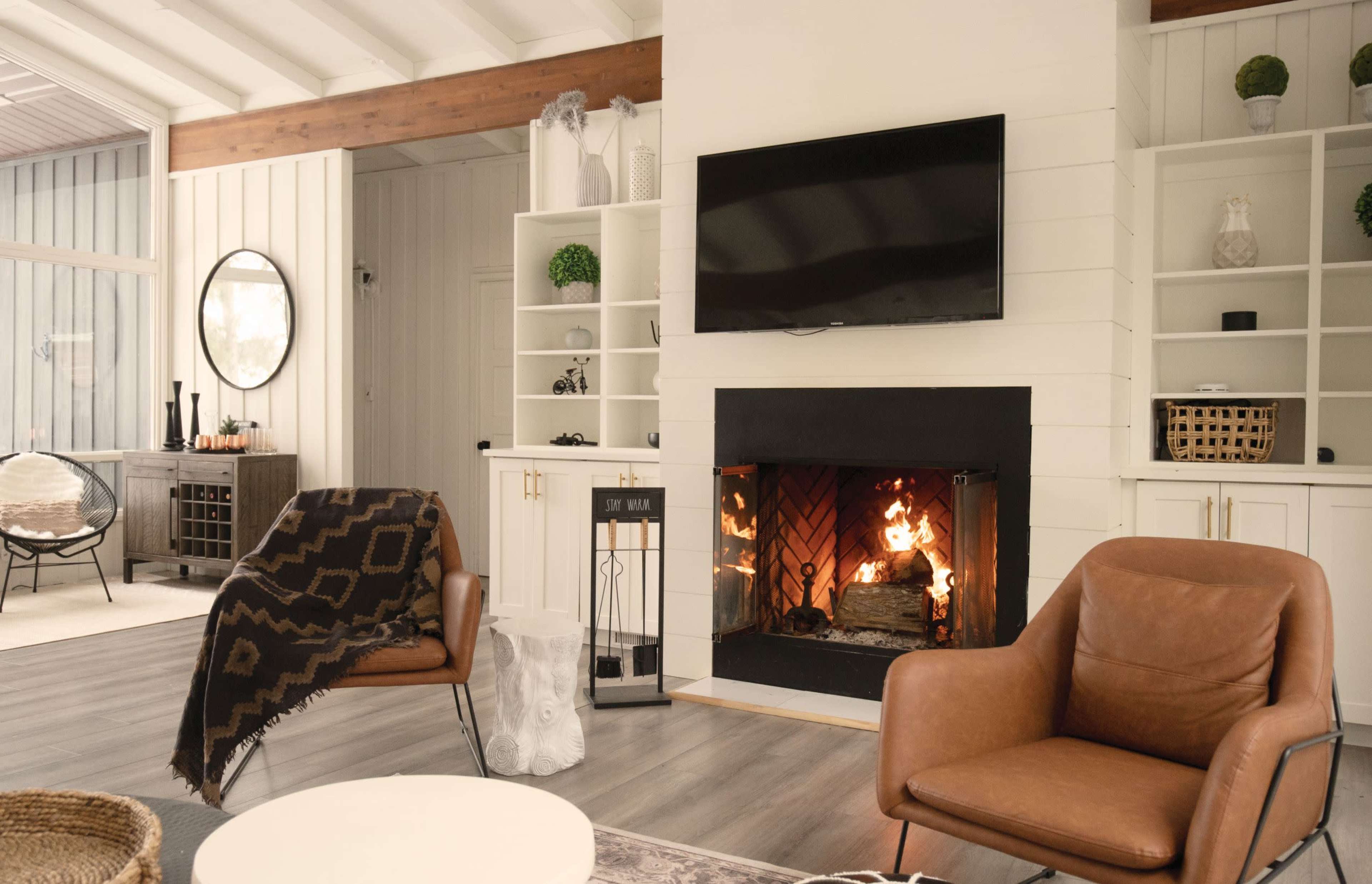 A cozy living room with a fireplace, two brown leather chairs, a round coffee table, and shelving units displaying decorative items.