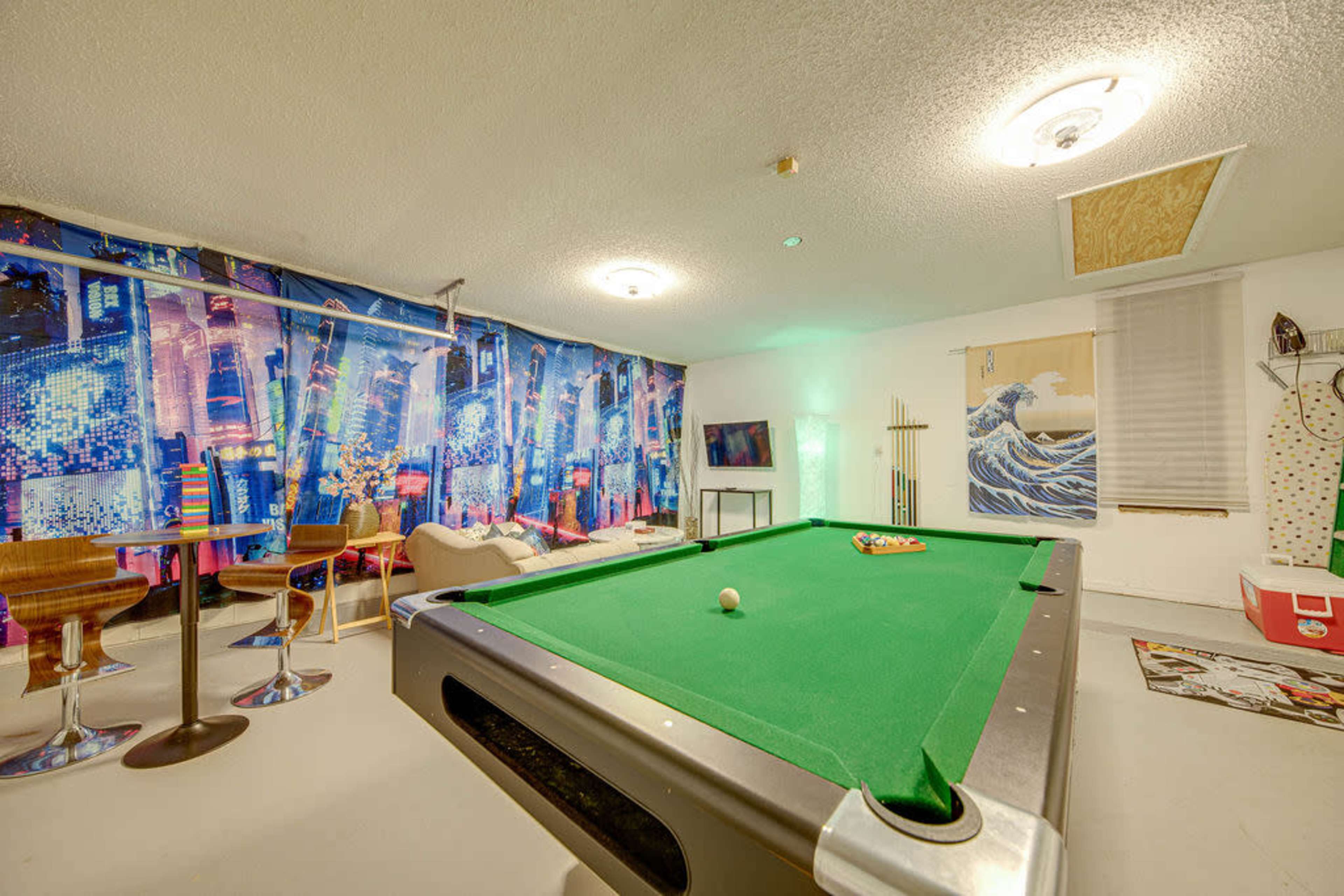 A pool table is positioned in a room with colorful wall murals, modern seating, and a television.