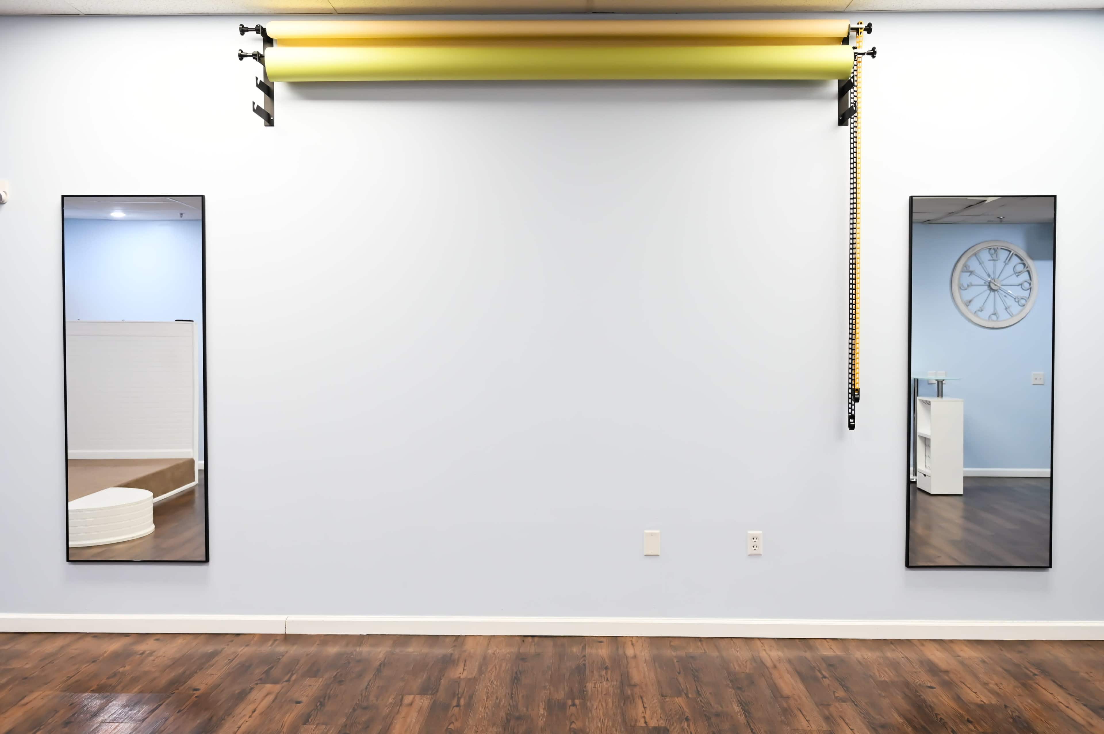 A light blue wall with two vertical mirrors, a row of colored rolls suspended above, and a clock on the right side.