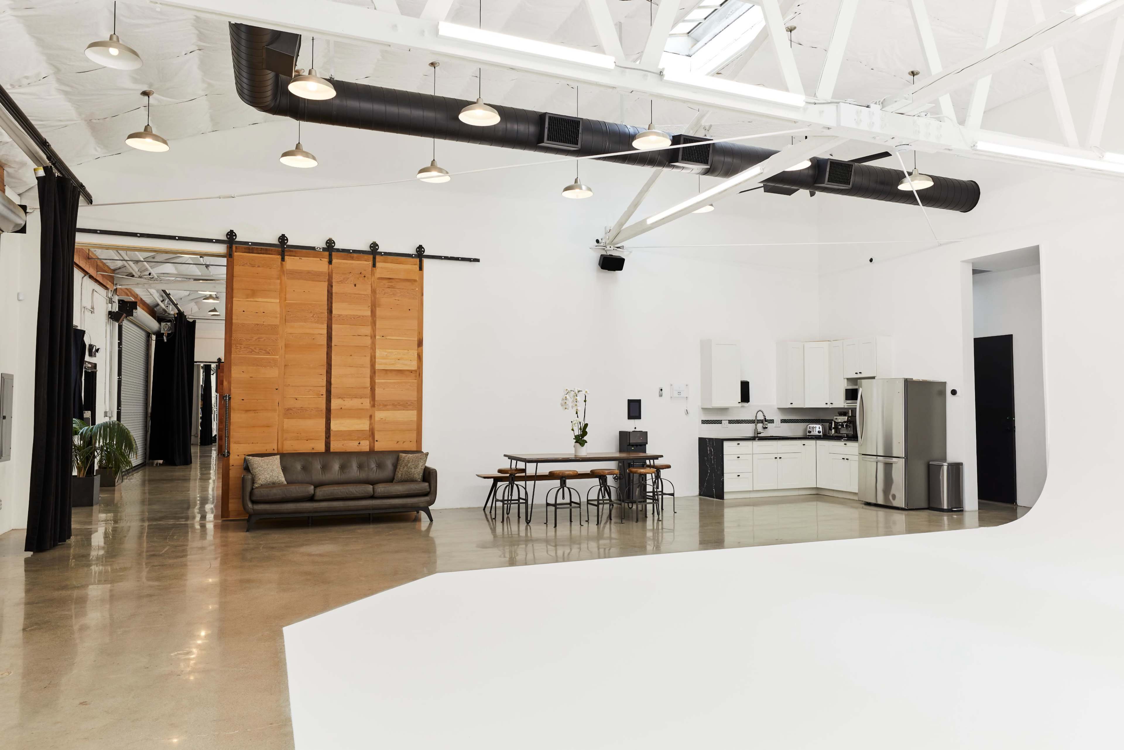 A spacious, brightly lit interior features a kitchen with a dining table, a sofa, and wooden sliding doors.