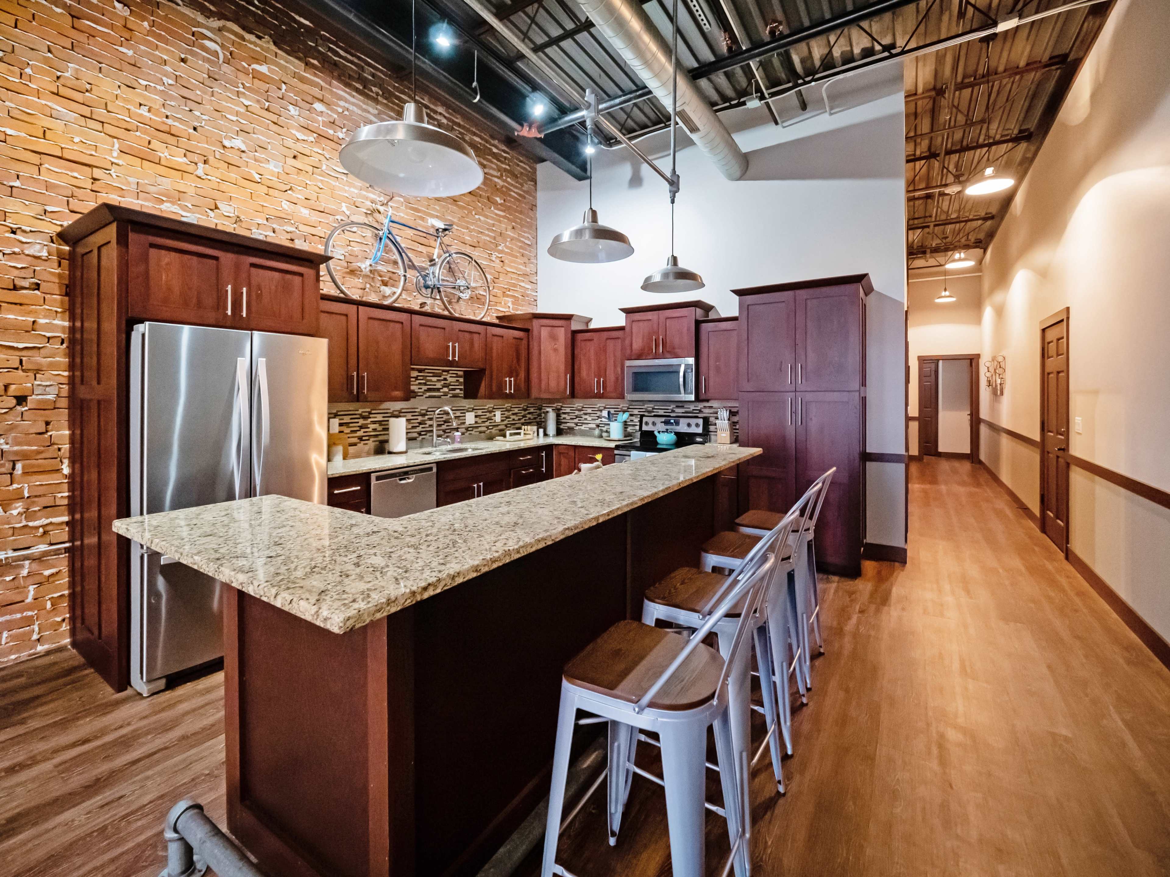 A modern kitchen featuring dark wooden cabinets, a granite countertop, and stainless steel appliances, with a bicycle mounted on the wall above.