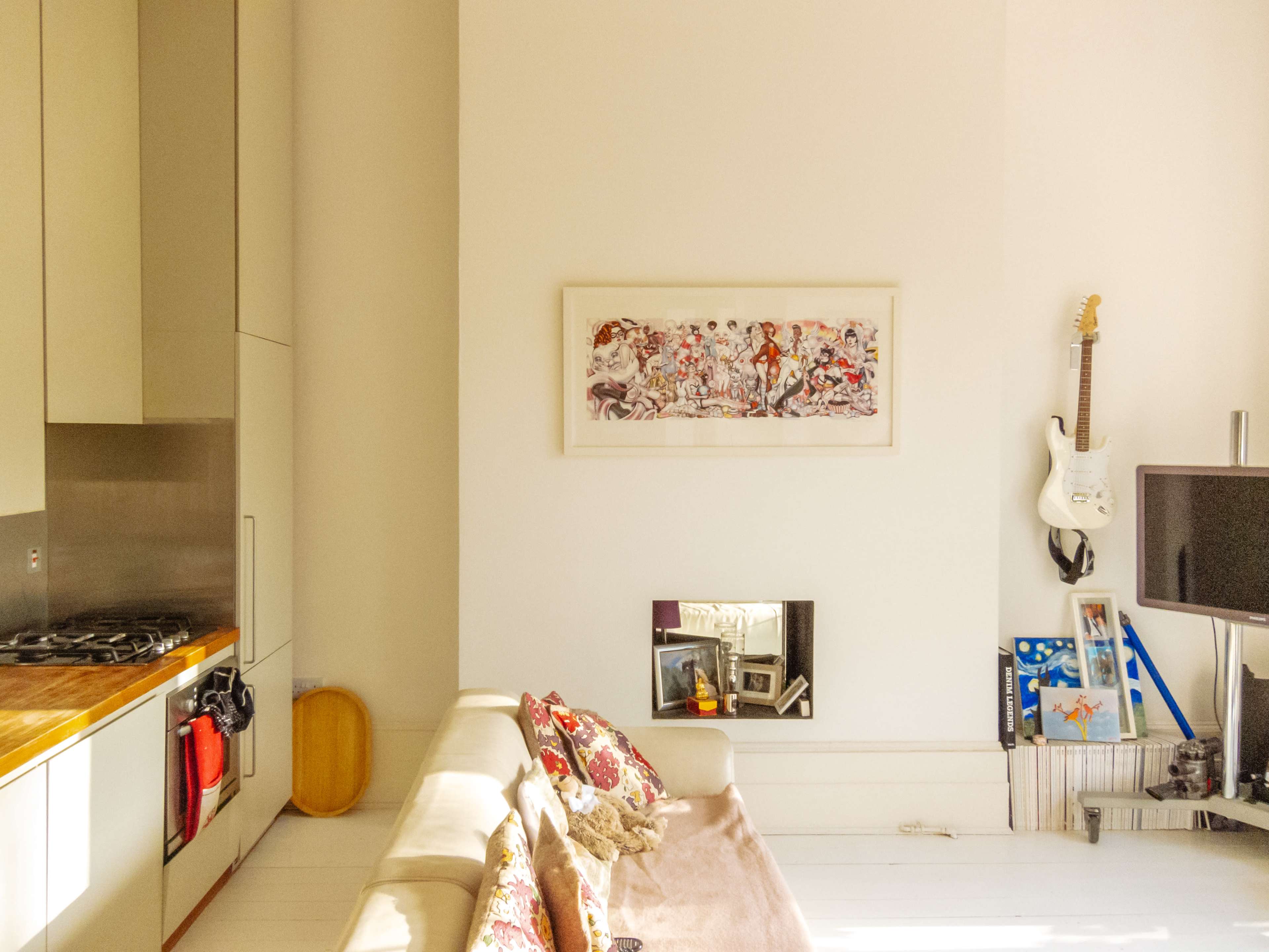 A living room features a beige sofa with decorative pillows, a wall-mounted television, and a framed artwork above a small mirror.