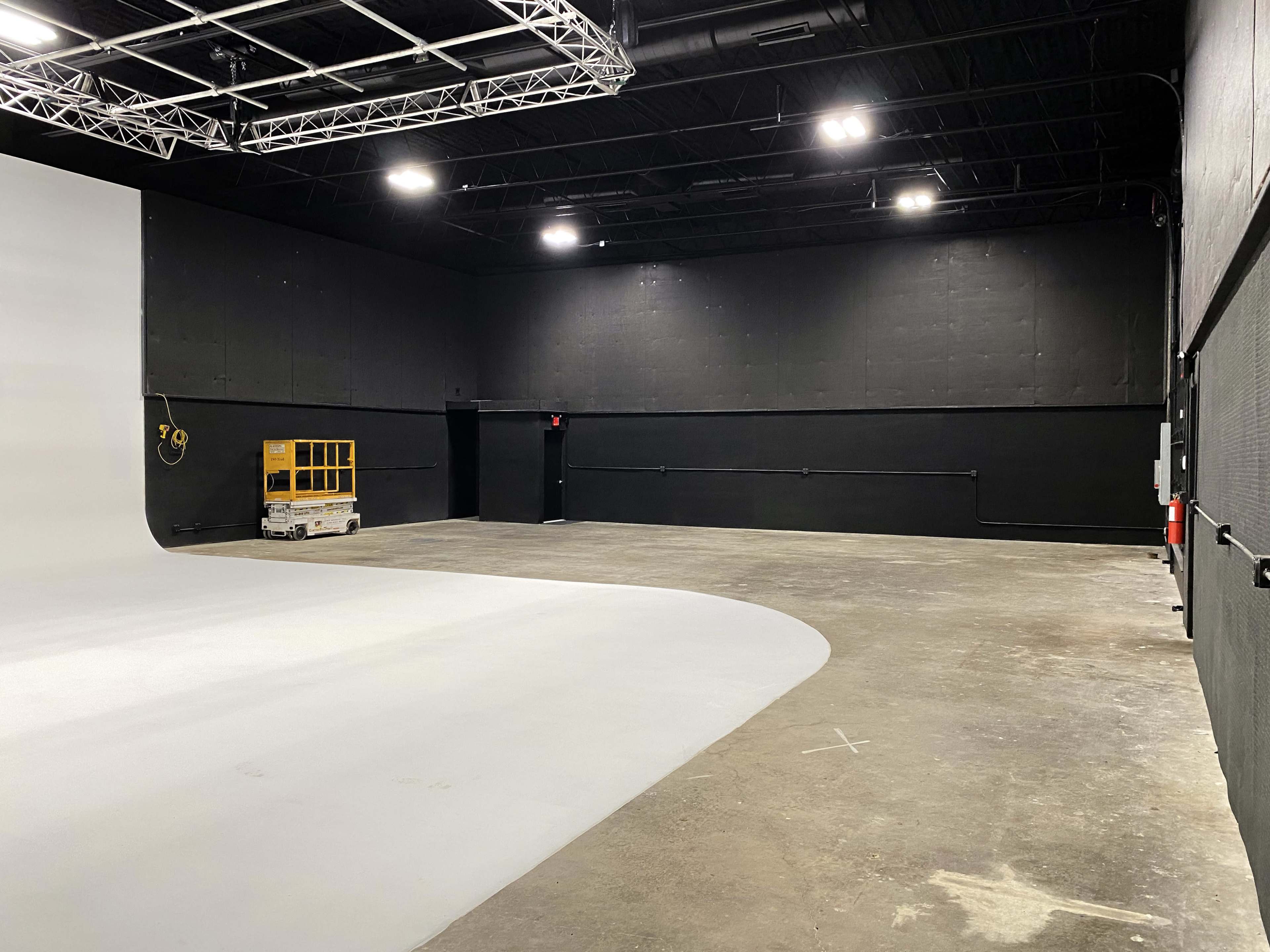 A photography studio features a gray seamless backdrop and a spacious black-walled area with minimal equipment.