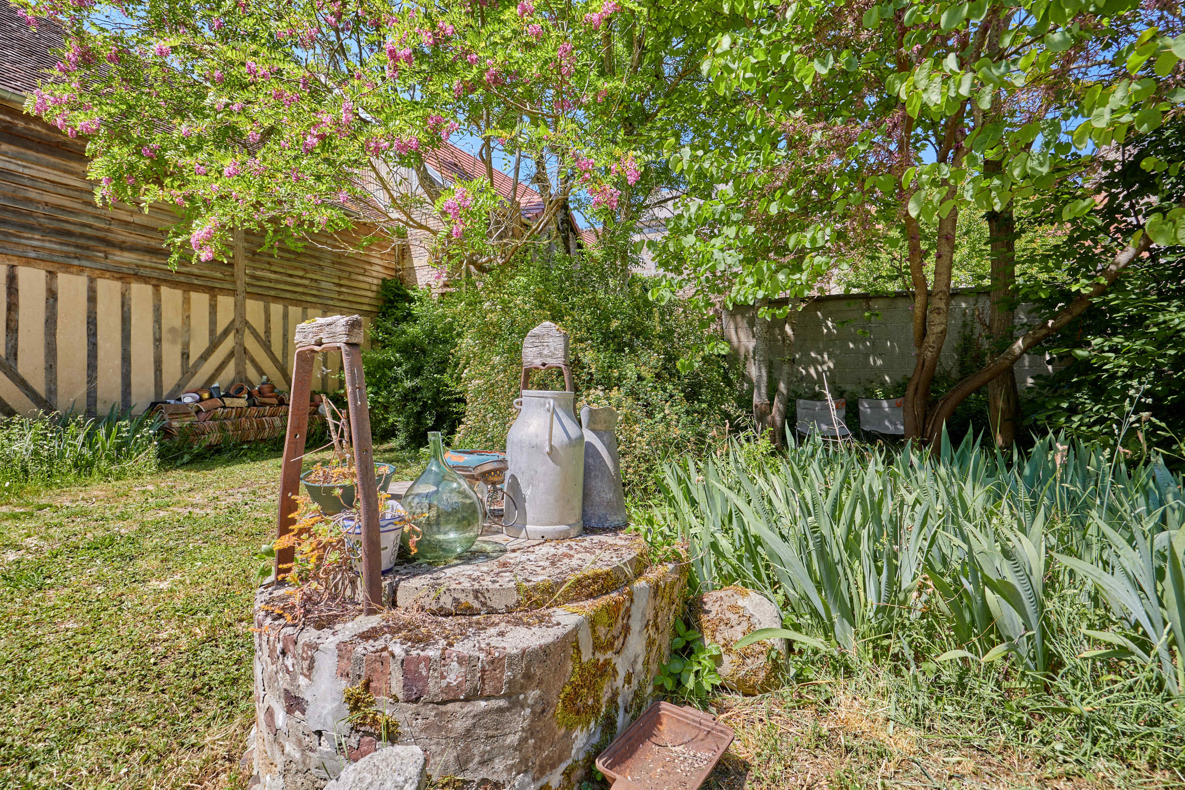 A rustic stone well is surrounded by flowering trees and greenery in a quaint garden setting.