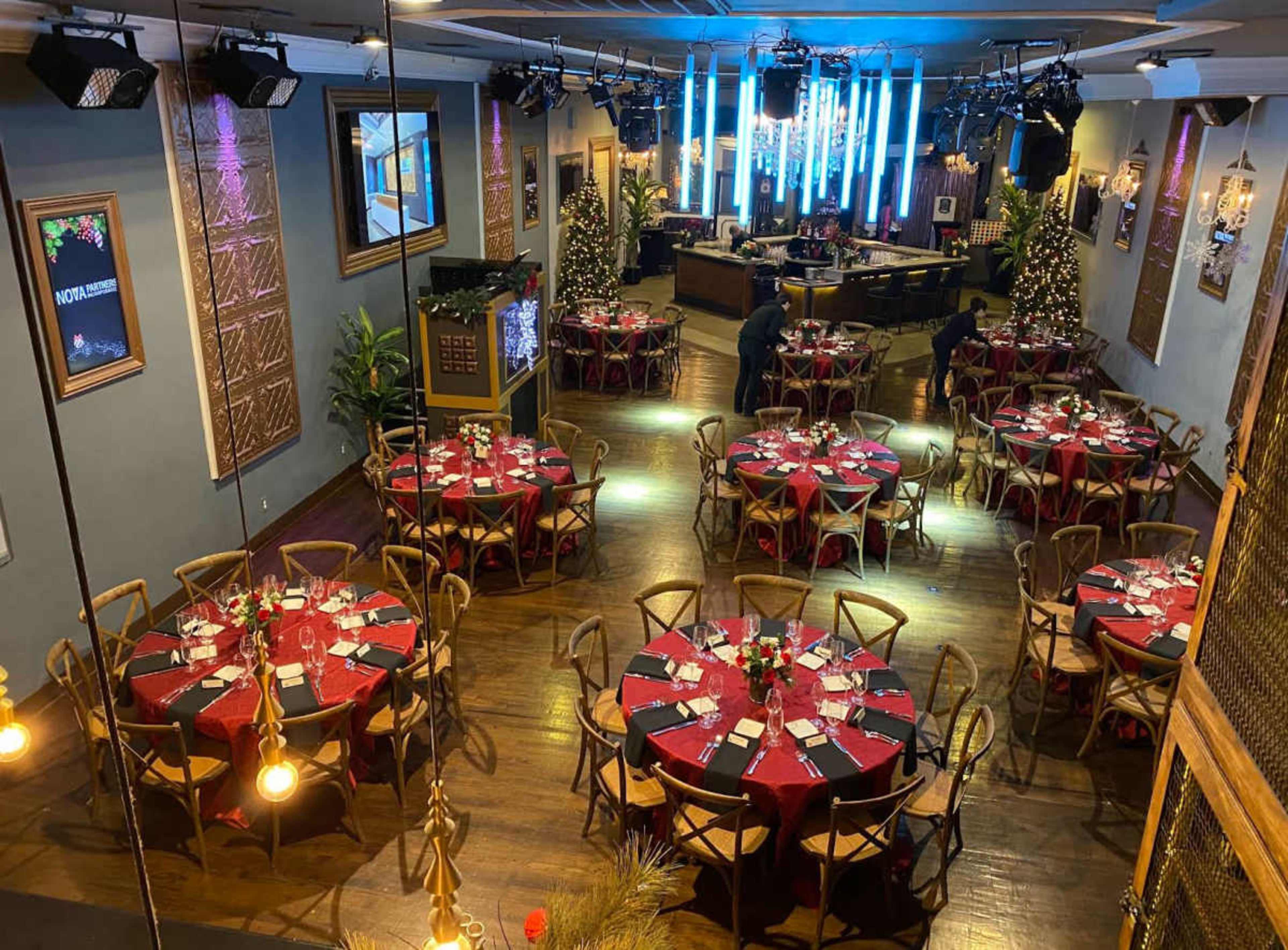 The image shows a spacious restaurant setting with multiple round tables dressed in red tablecloths, arranged neatly in a well-lit room decorated for a festive occasion.