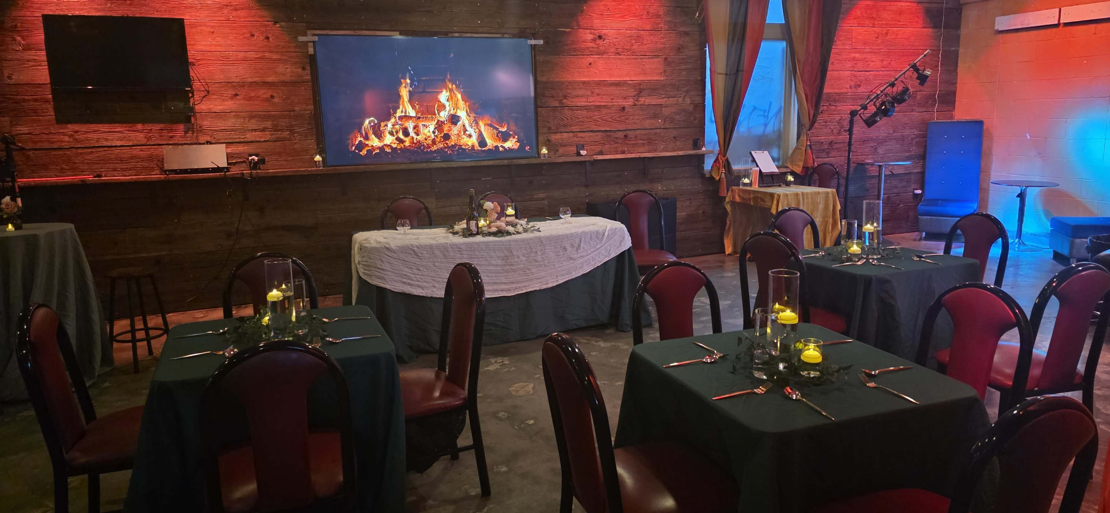 A dining area with several tables set for a meal, featuring a decorative fireplace display on the wall, illuminated by soft lighting.