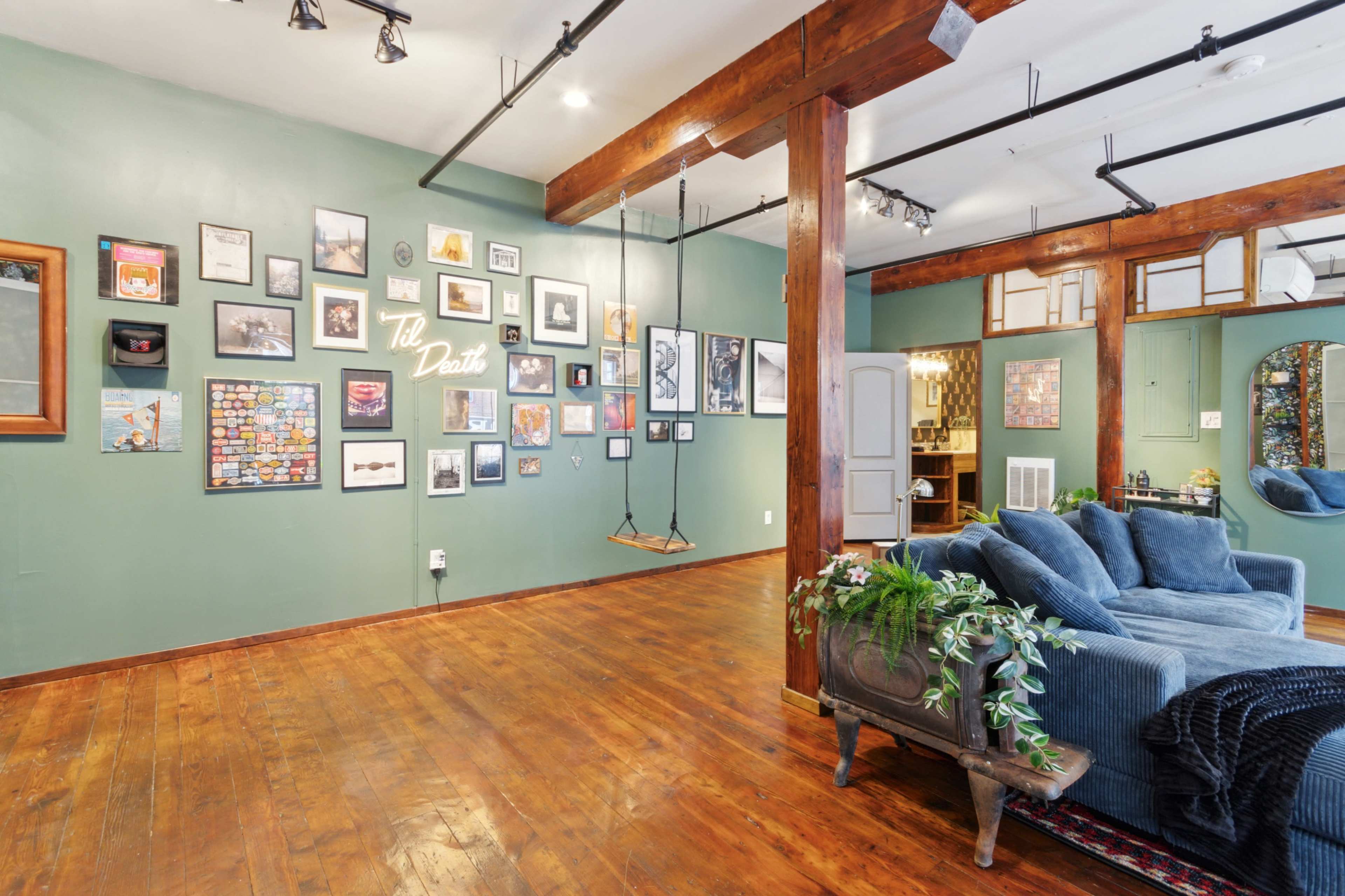 A room with green walls adorned with various framed pictures, wooden beams on the ceiling, and a blue couch in a corner.