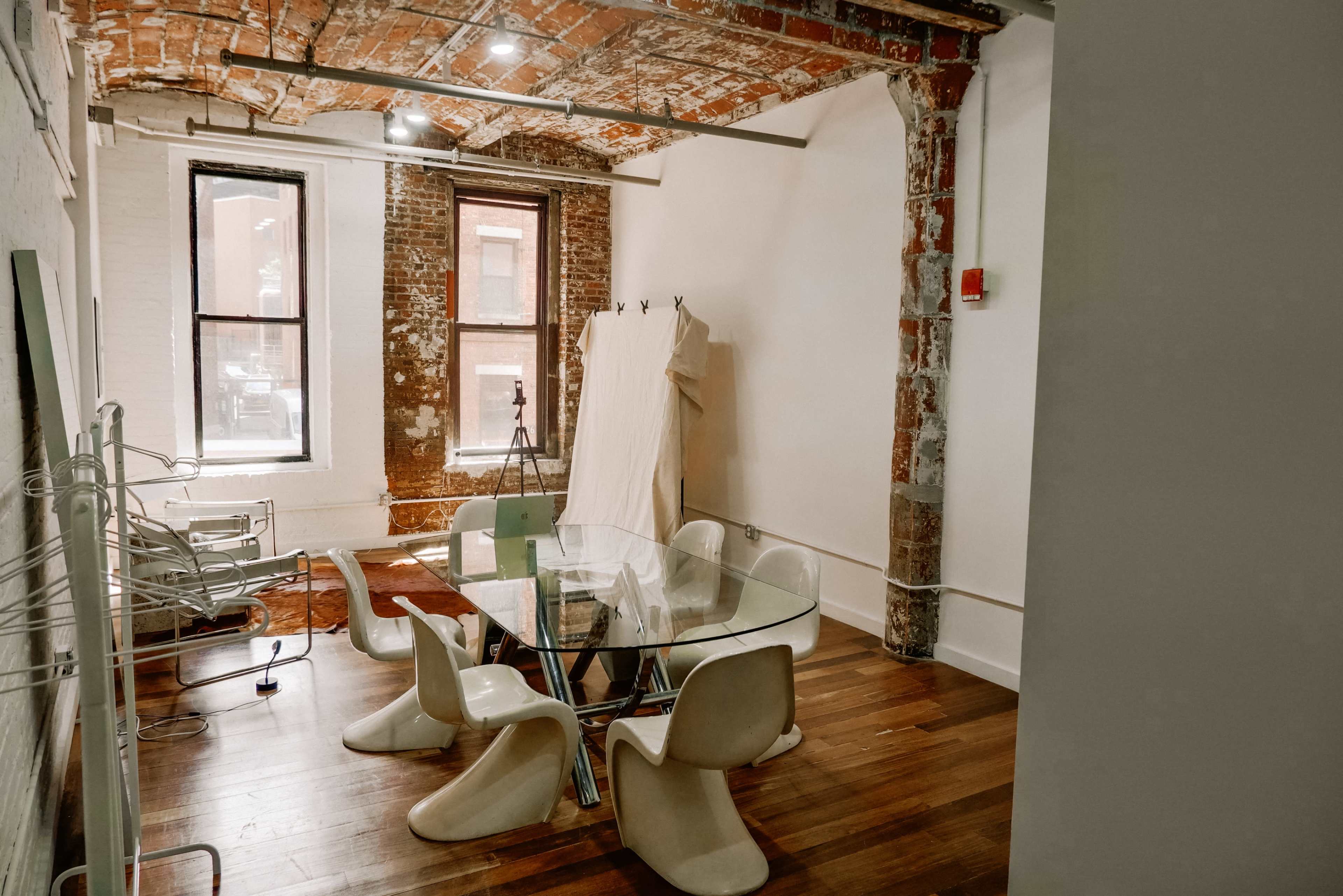 A modern meeting room featuring a glass table surrounded by sculptural chairs, with exposed brick walls and large windows.