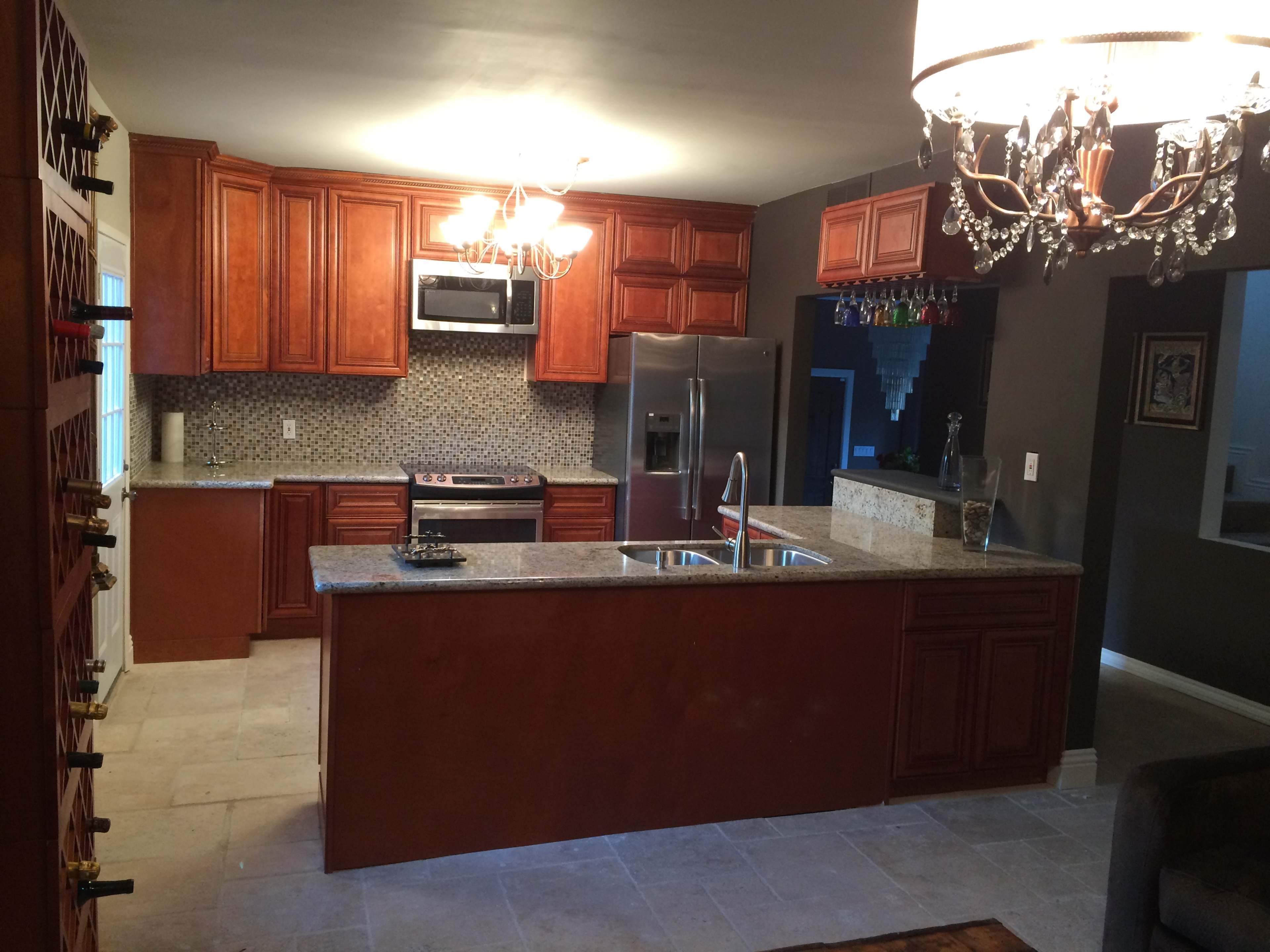 A kitchen with wooden cabinetry, stainless steel appliances, a granite countertop island, and mosaic tile backsplash.