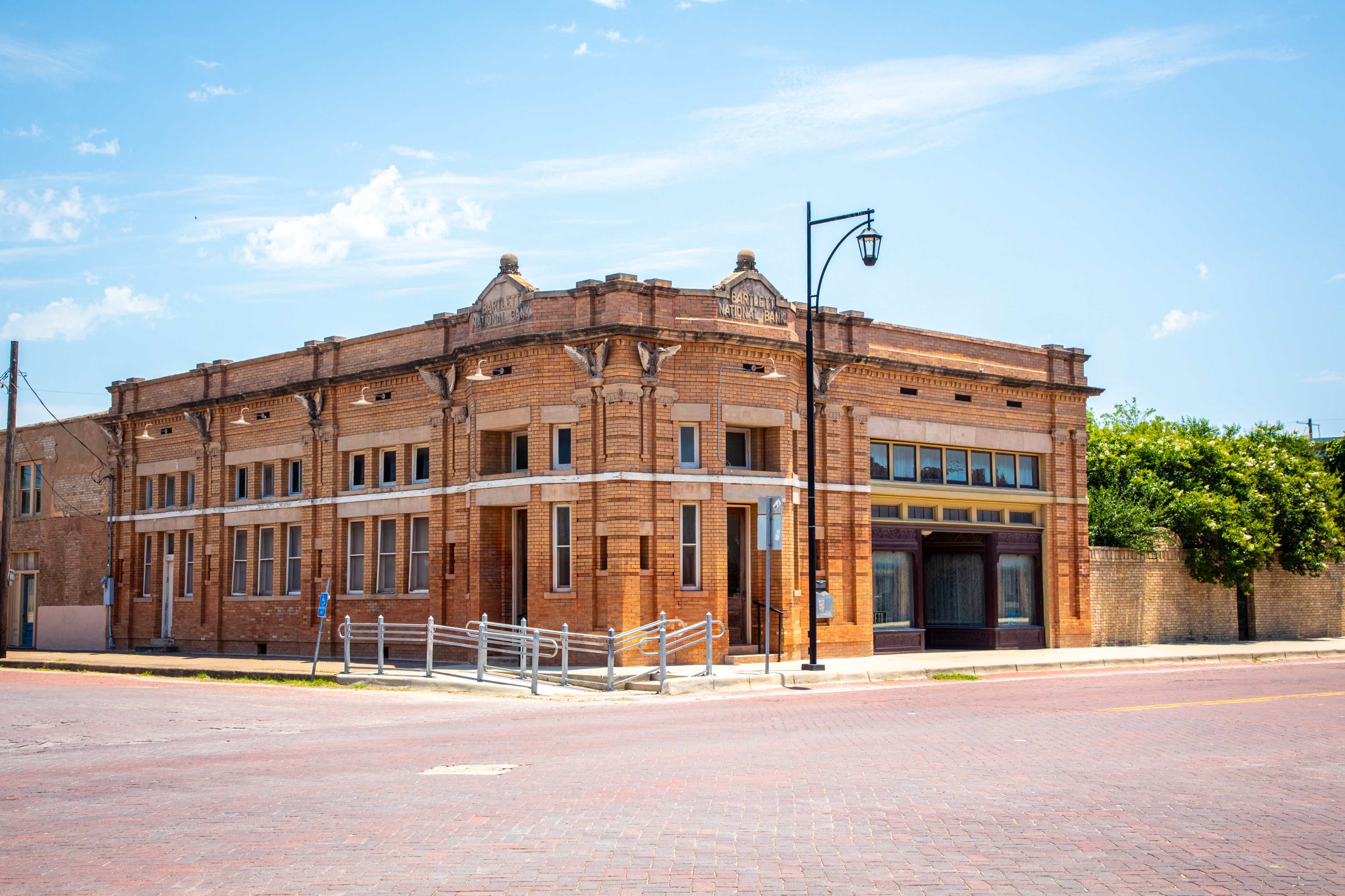 A historic brick building with decorative architectural features, situated at the corner of a street with a clear blue sky above.