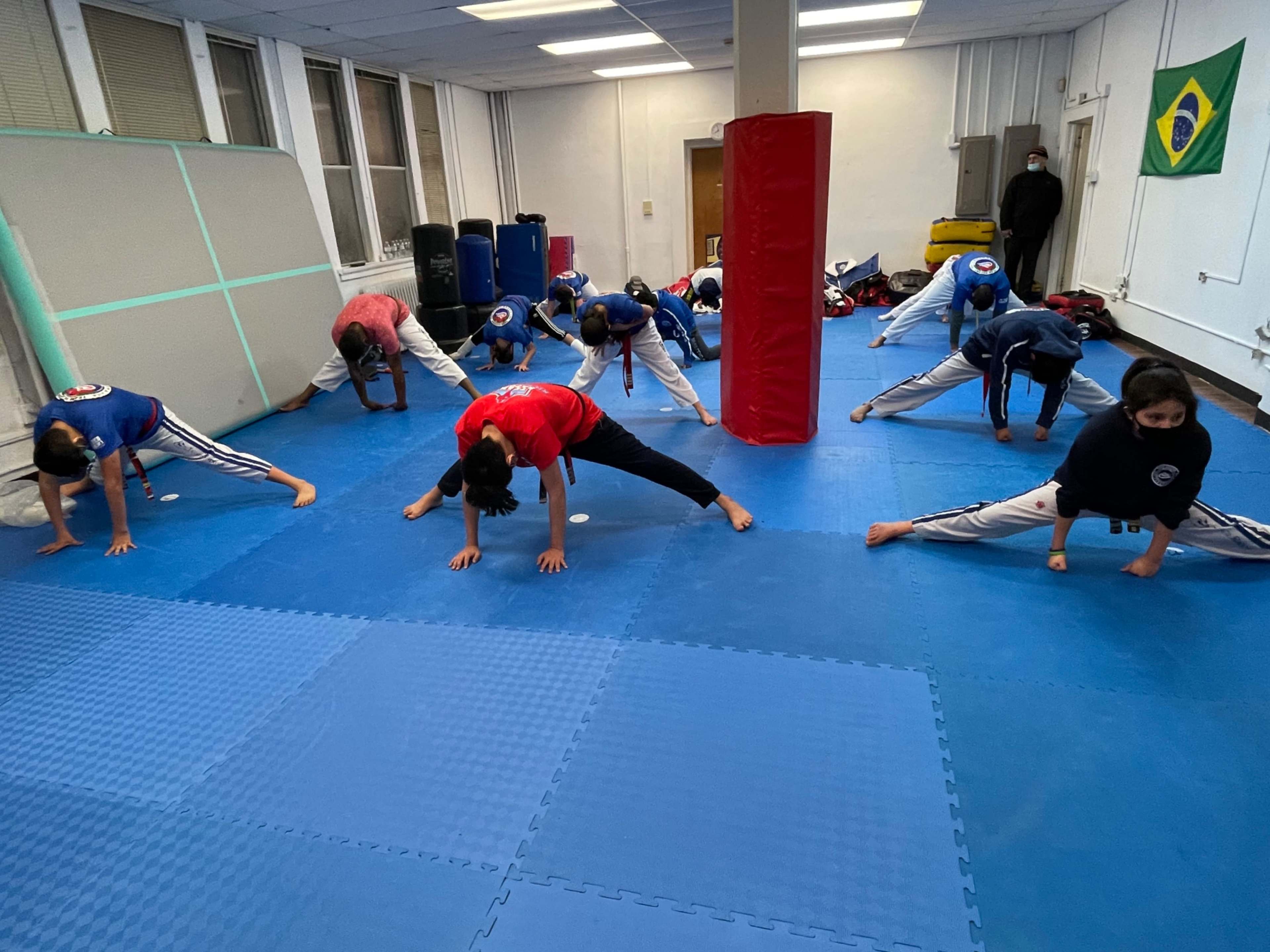 A group of individuals practice stretching exercises on blue mats in a training room.