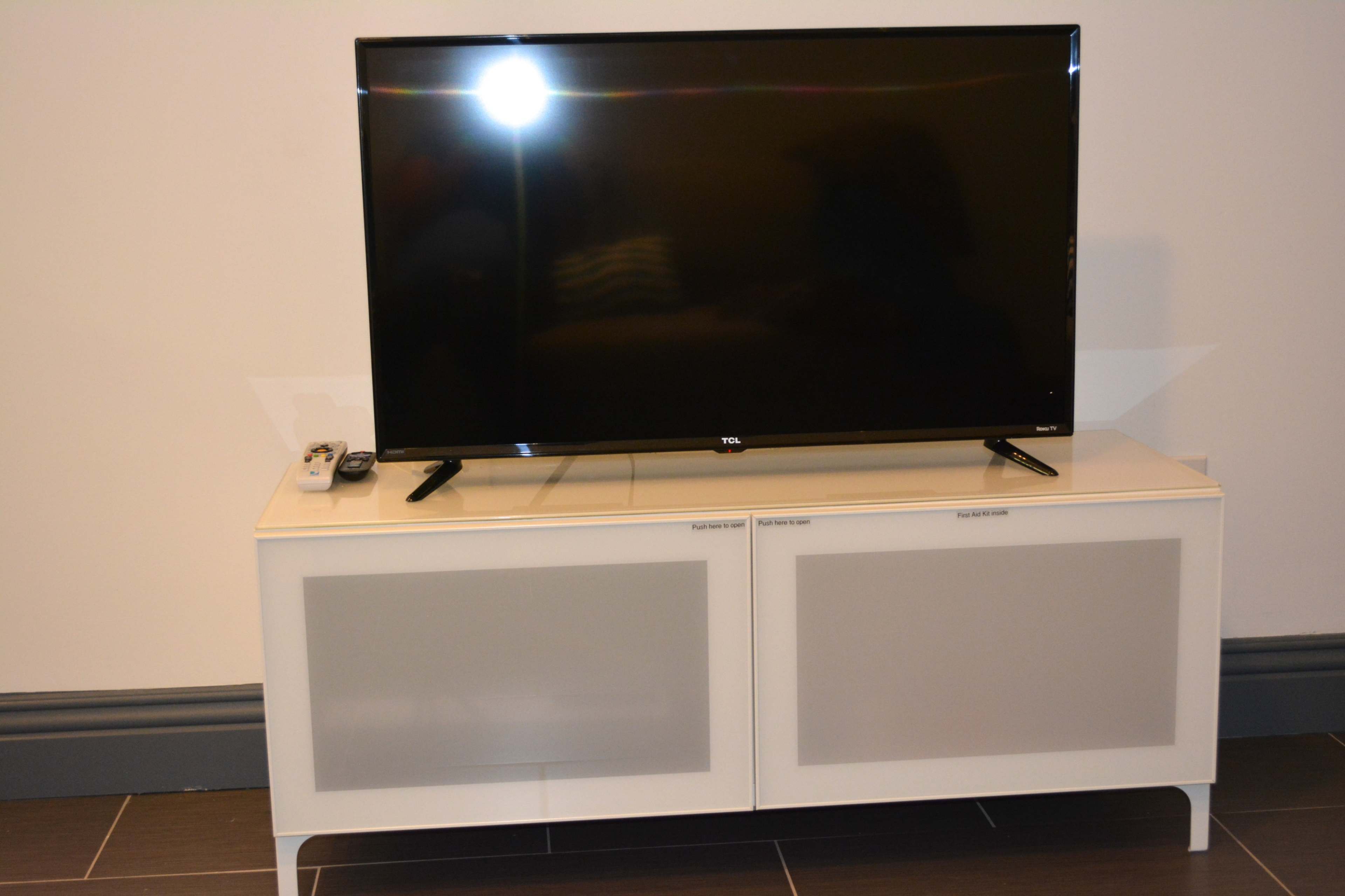 A black television is placed on a white media console with frosted glass doors and a remote control nearby.