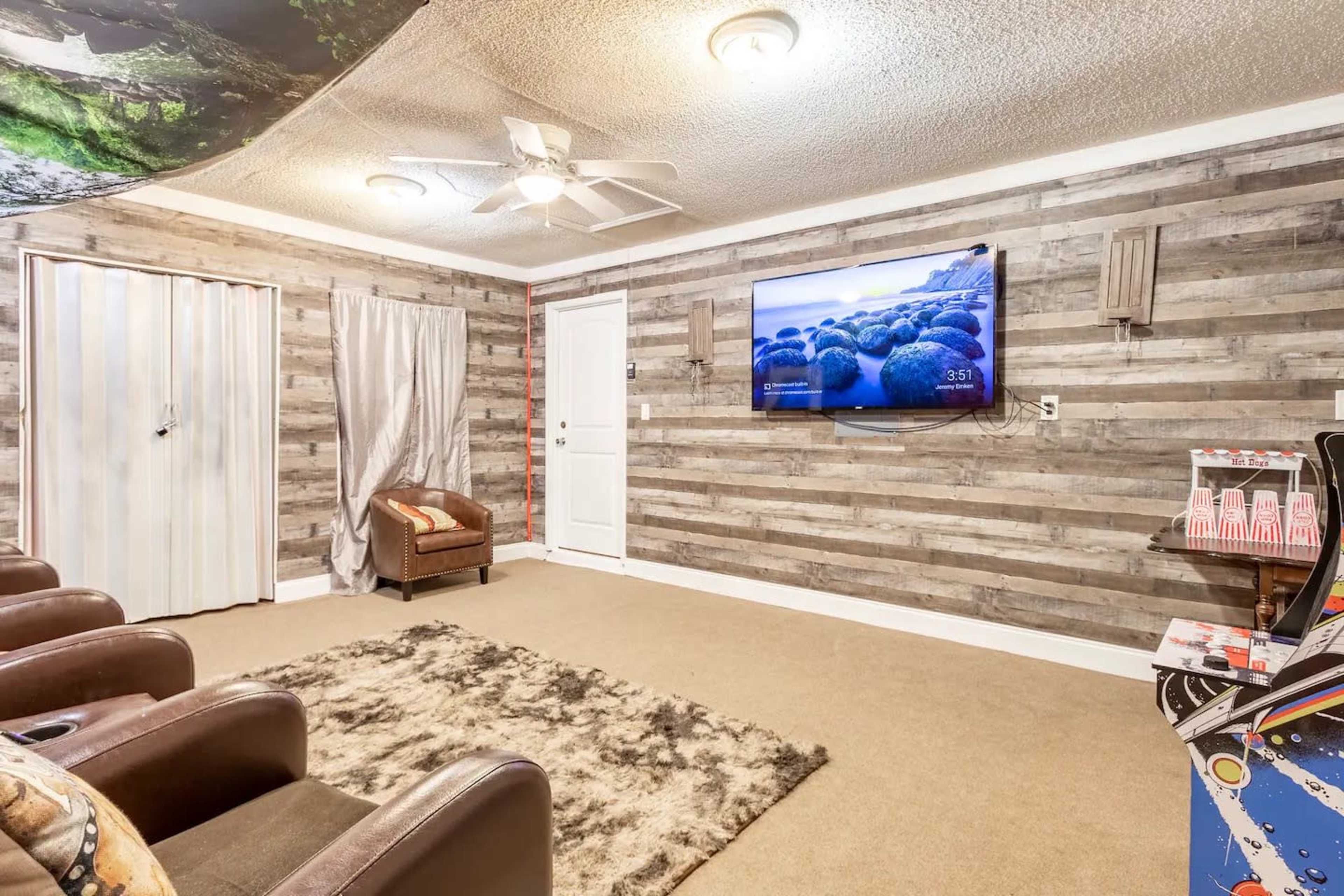 The room features a seating area with brown recliners, a wall-mounted television, and a patterned area rug on a light-colored carpet.