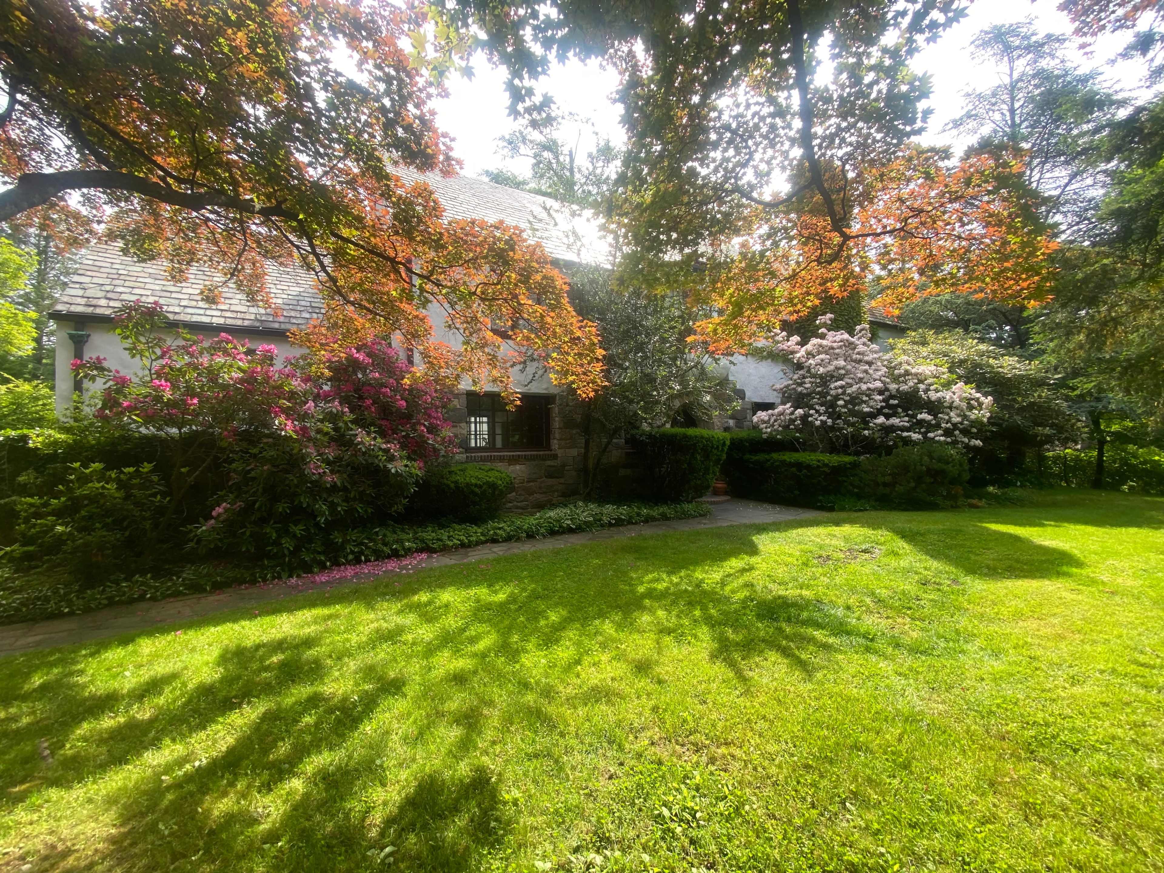 A well-maintained house is surrounded by colorful flowering bushes and a lush green lawn.