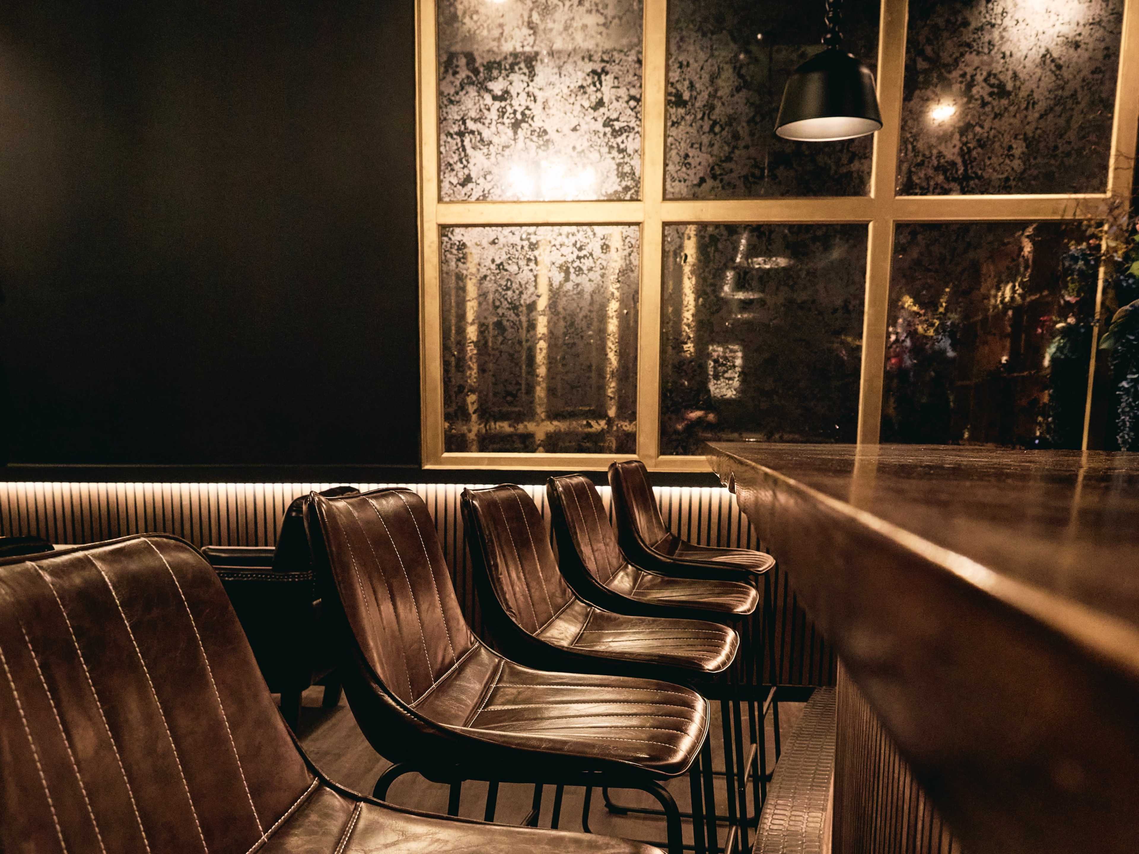 A row of leather chairs in front of a wooden bar, with a large, foggy window behind them.