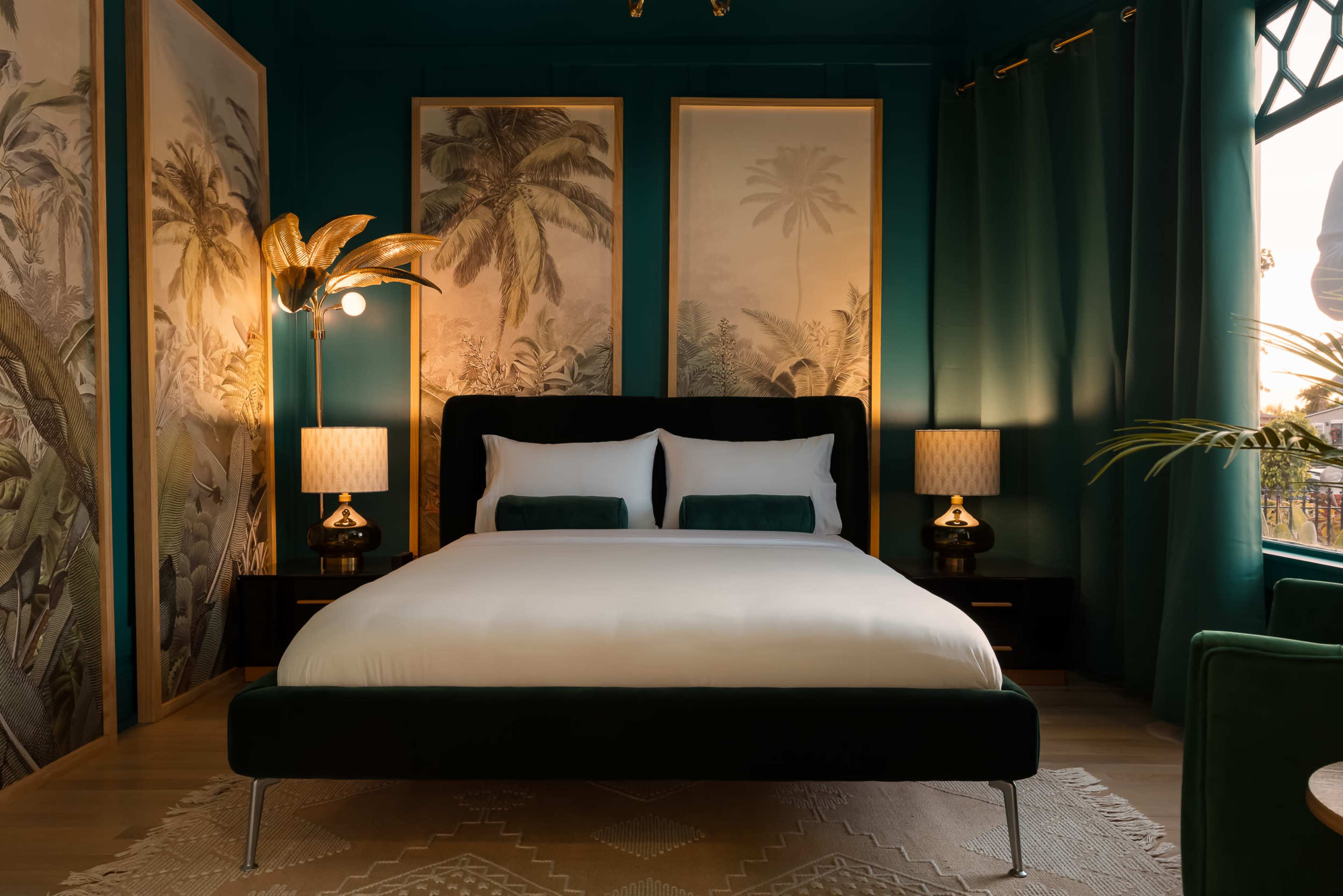 The image showcases a stylish bedroom with a large bed, palm-themed artwork on the walls, and decorative lamps on either side.