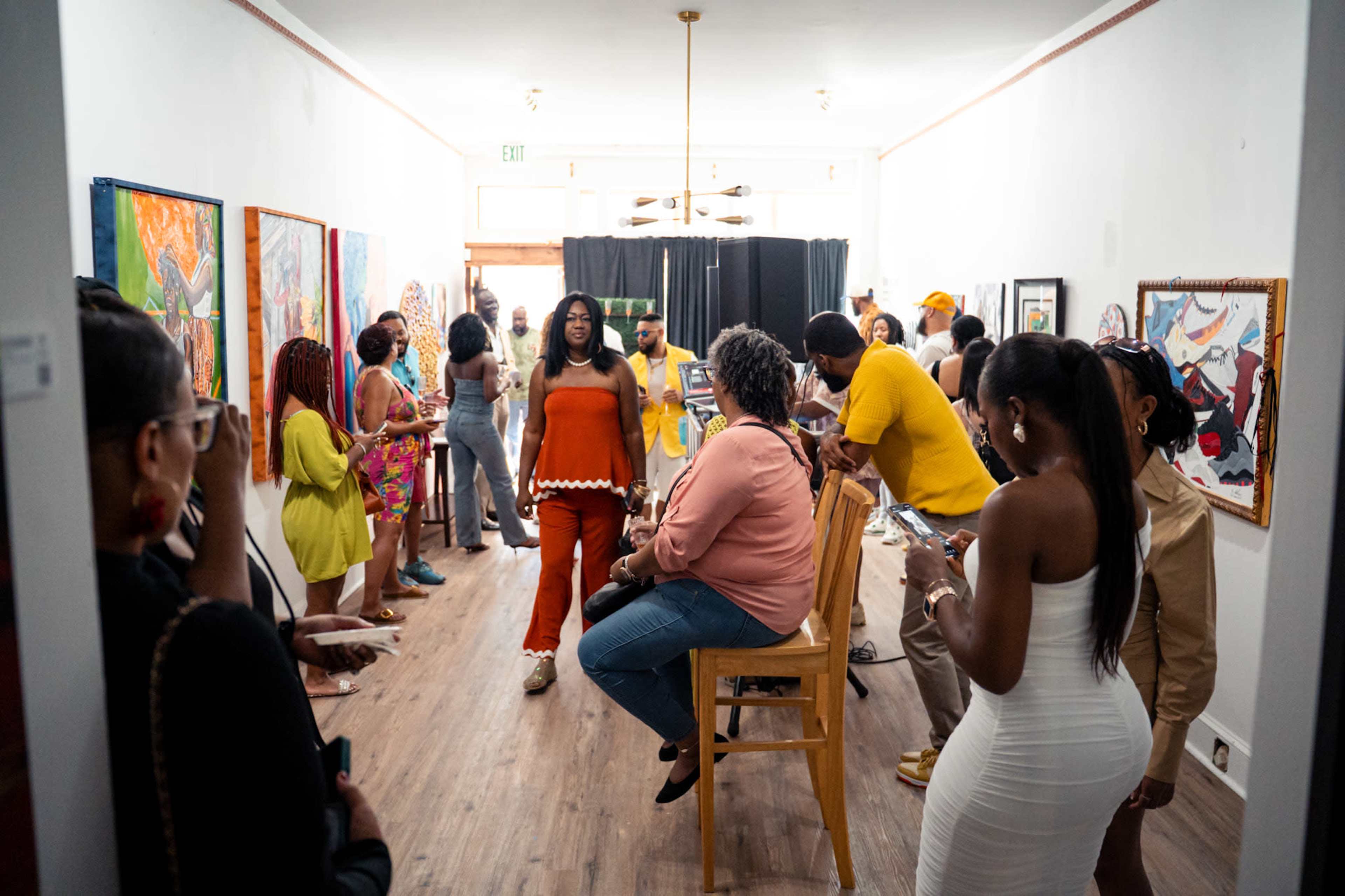 A diverse group of people gathers in an art gallery, with some observing artwork and others engaging in conversation.