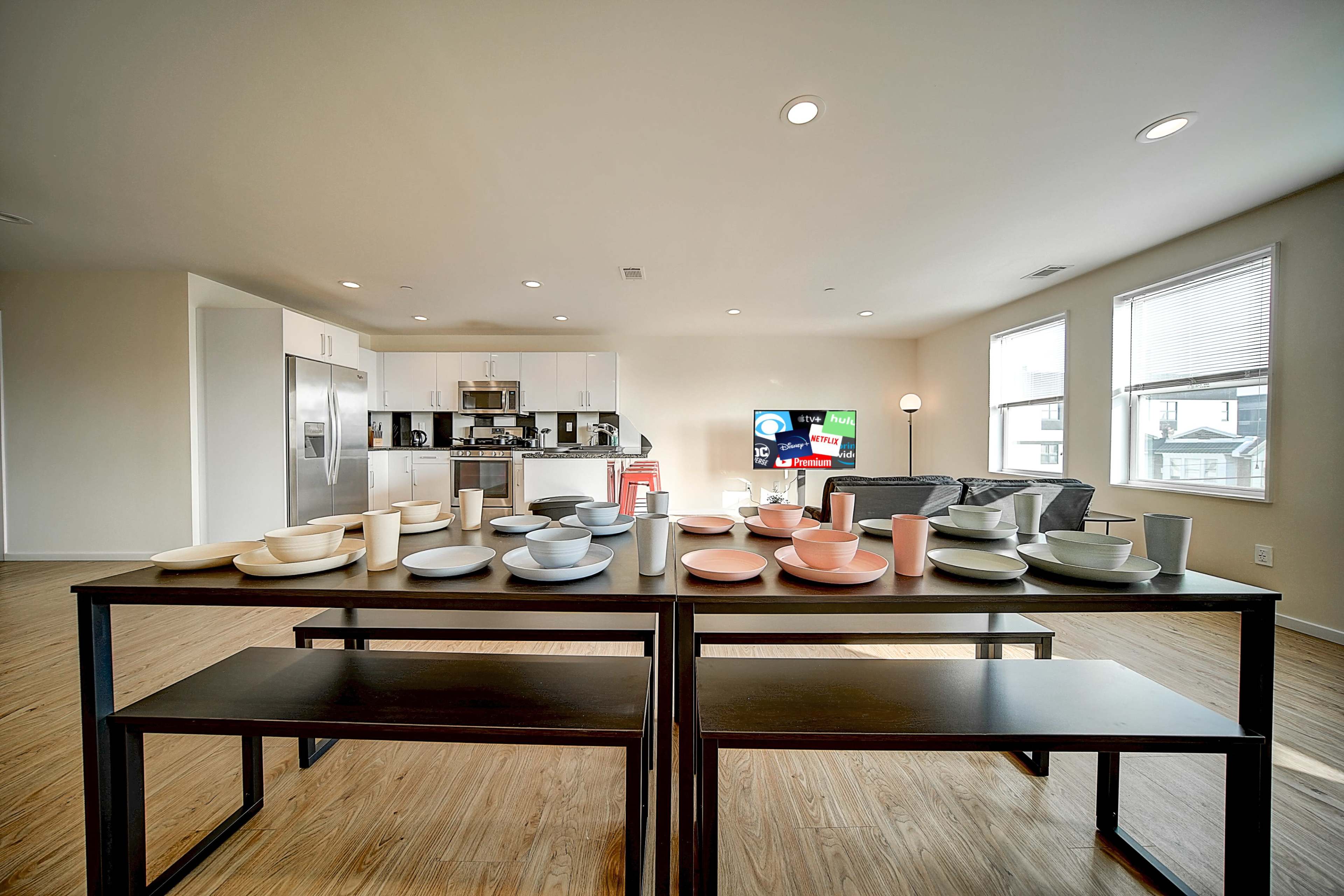 A dining table is set with various plates and cups, positioned in a modern kitchen and living area with light-colored walls and wooden flooring.