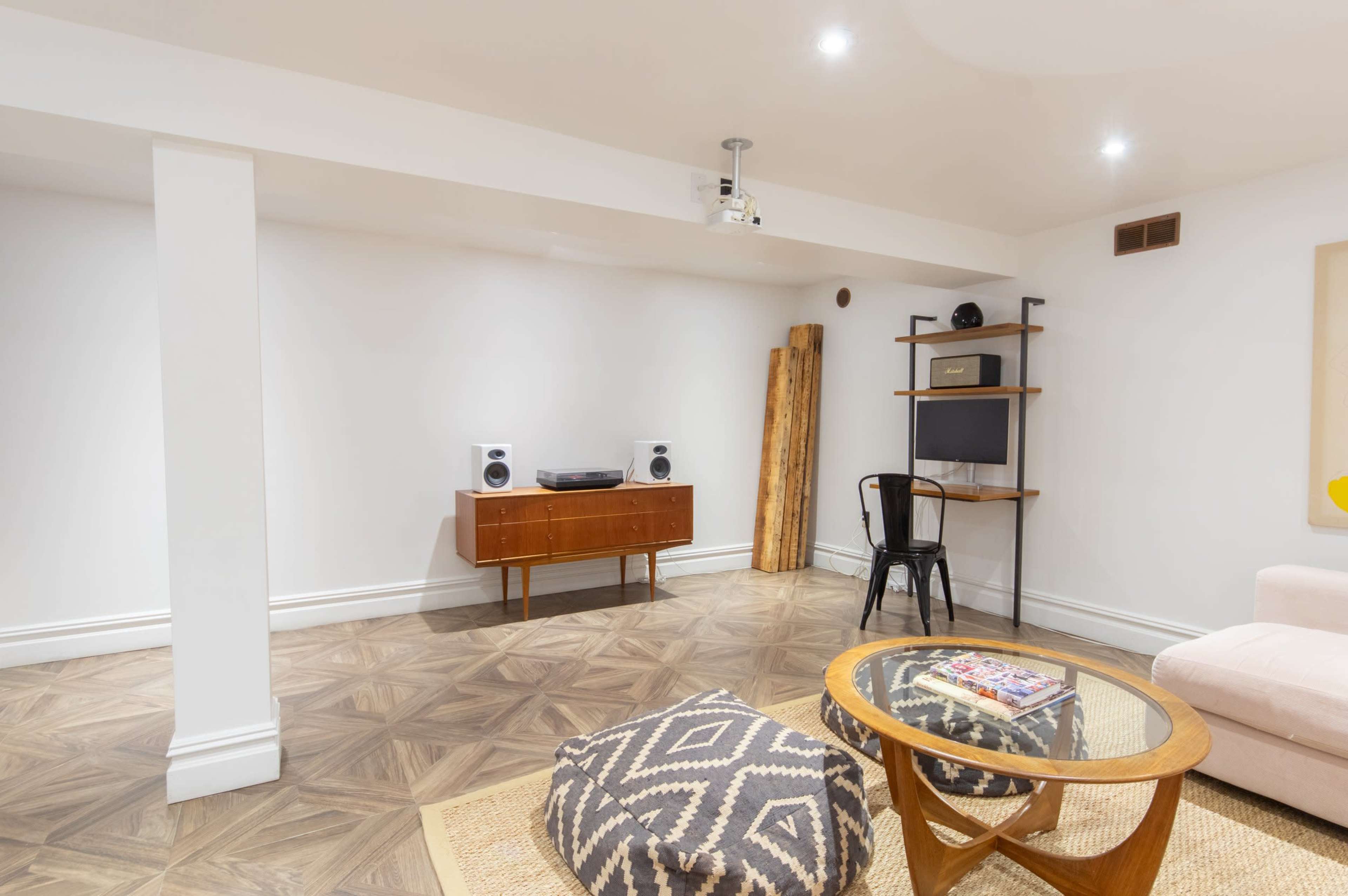 A modern basement room features a wooden console, a television on a stand, speaker units, and a low coffee table with decorative items.