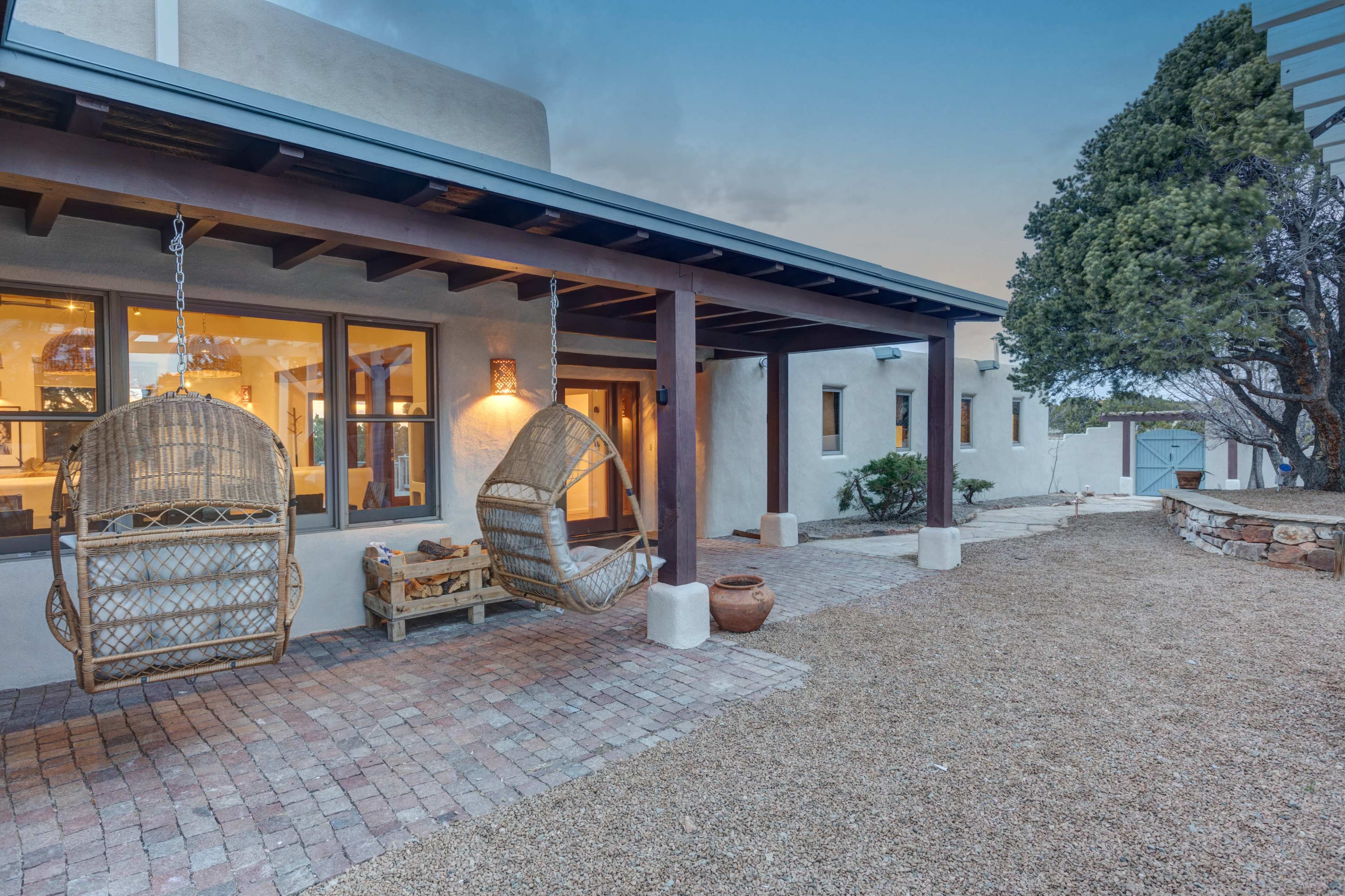 The image features a southwestern-style home with two hanging wicker chairs on a porch, surrounded by a gravel pathway and landscaped shrubs.