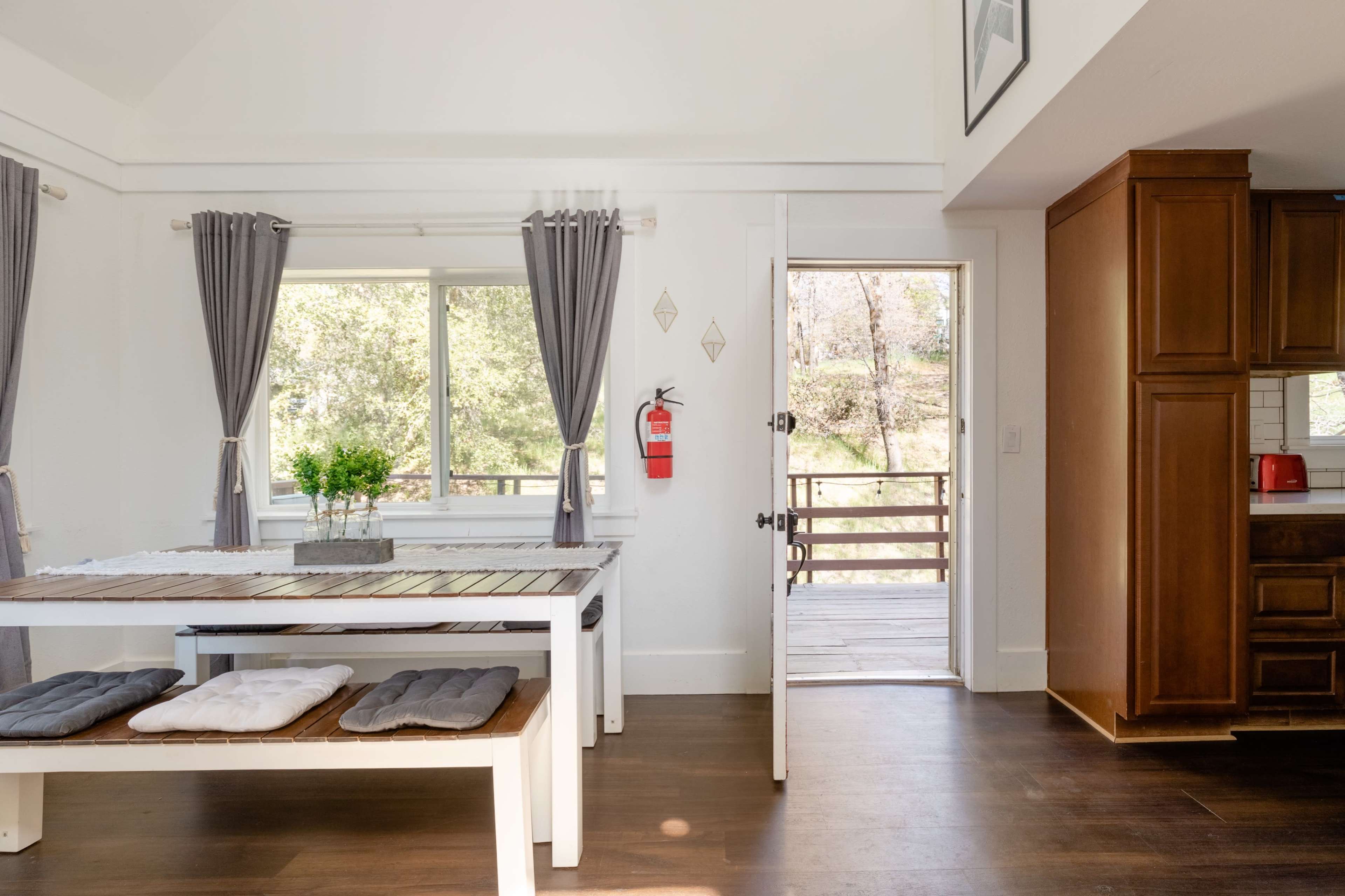A spacious dining area features a long wooden table with bench seating and is connected to an outdoor deck through an open door.