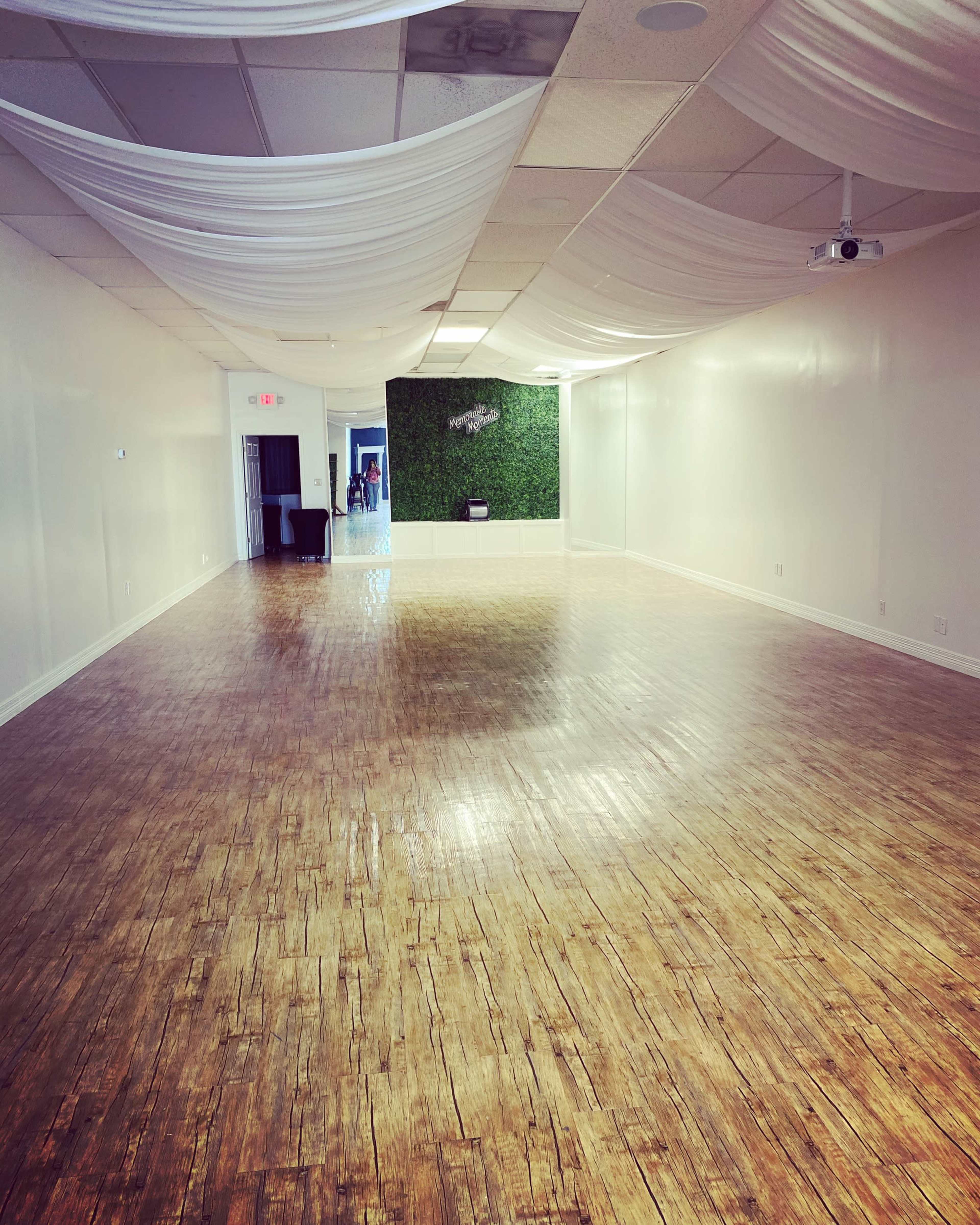 The image shows a spacious room with wooden flooring, white walls, and decorative drapery on the ceiling.