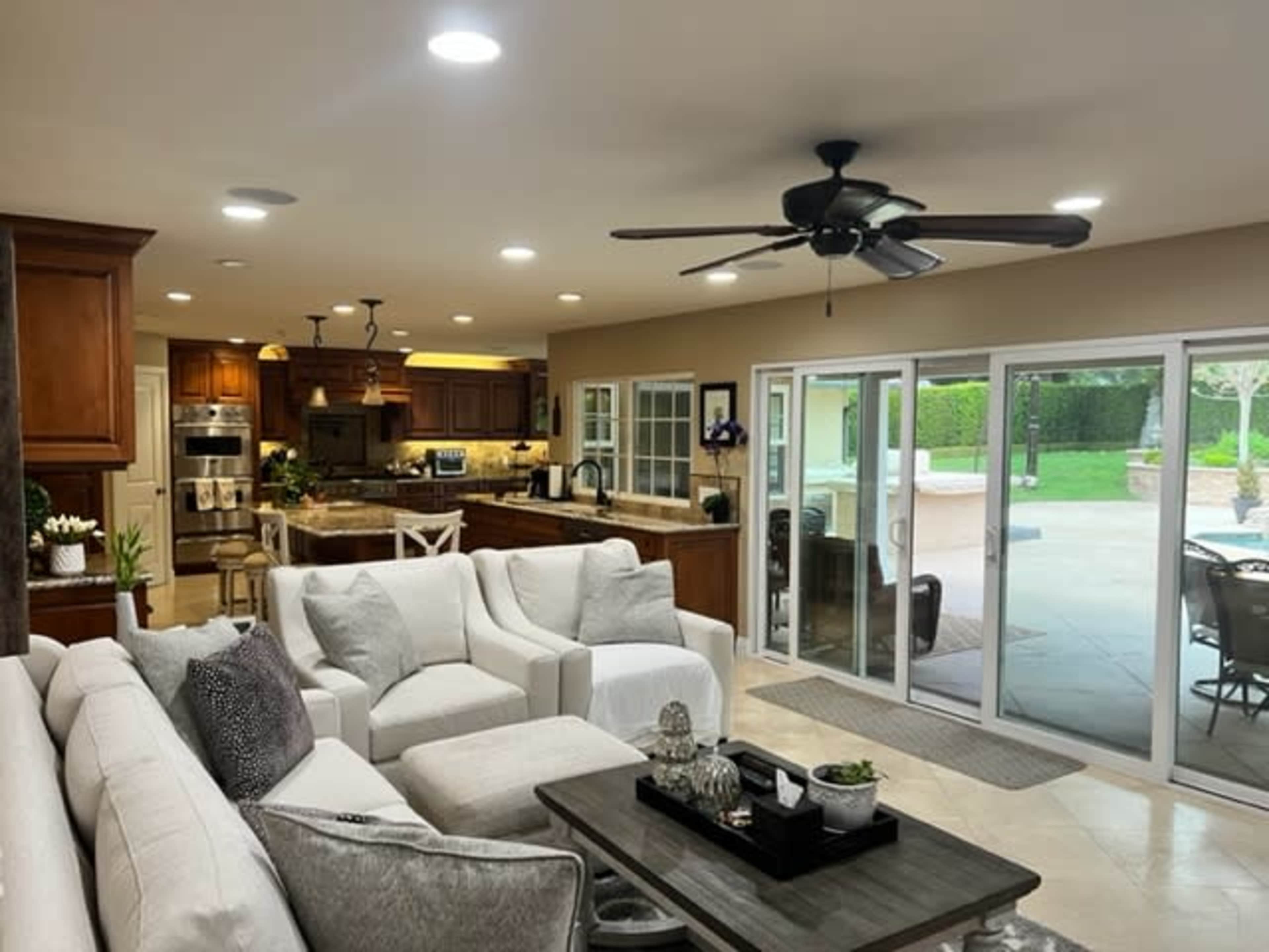 A spacious, modern living area features a light-colored sofa set, a coffee table, and a view of an outdoor patio through sliding glass doors.