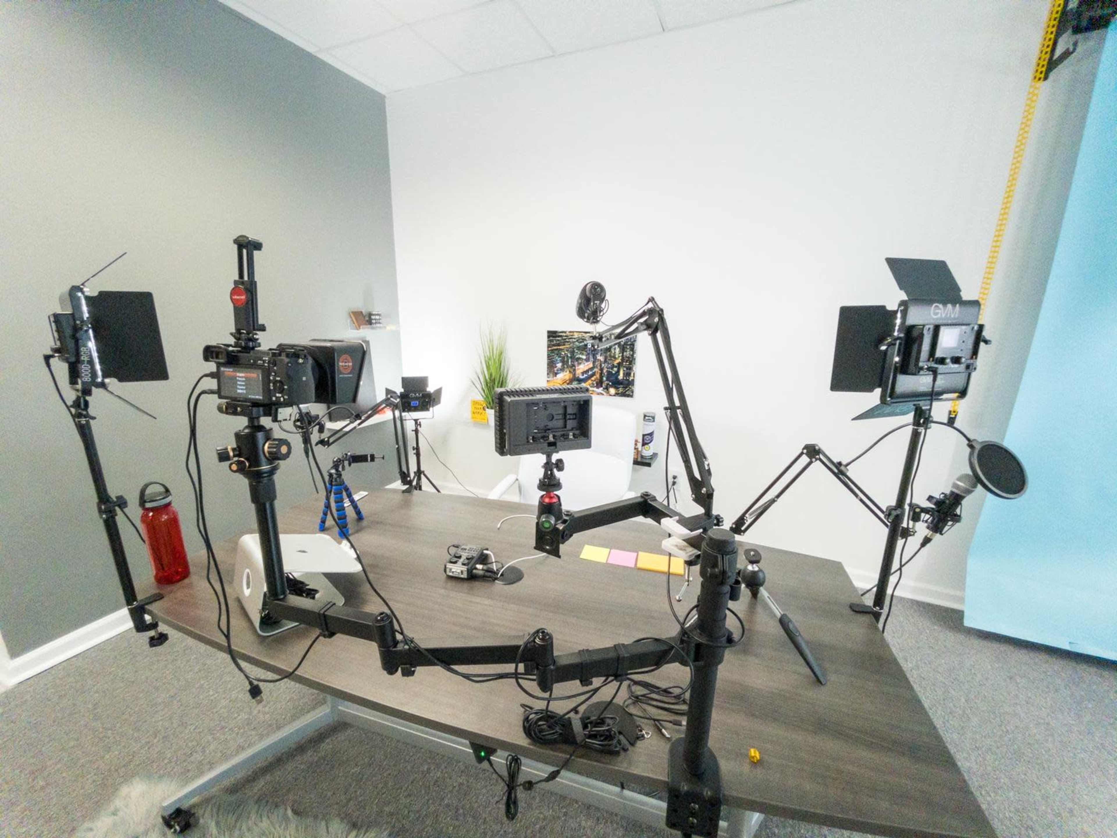 A workspace equipped with cameras, lighting equipment, and a computer setup on a wooden table.