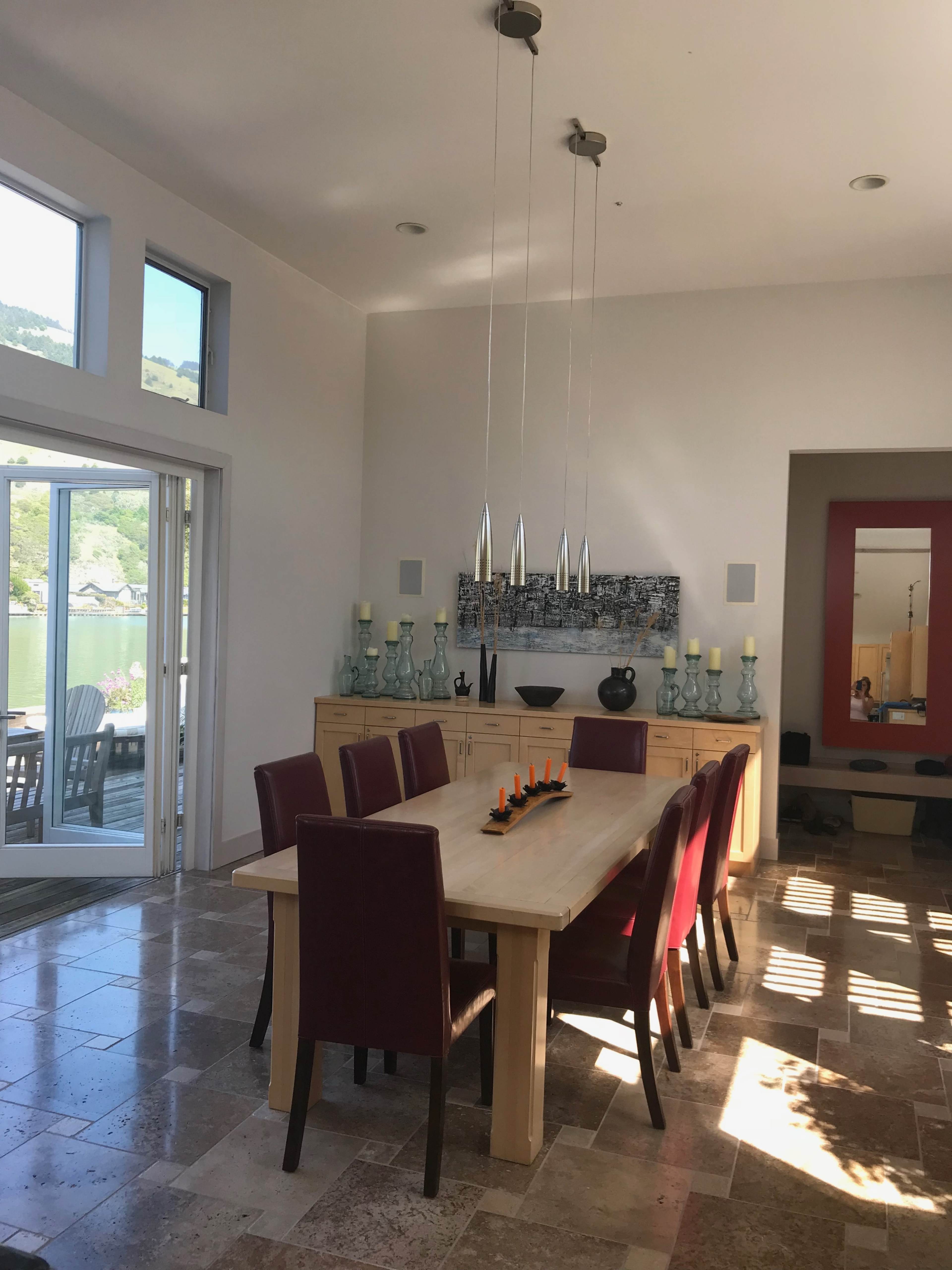 A modern dining room with a long wooden table surrounded by red chairs, large windows, and decorative items on a sideboard.