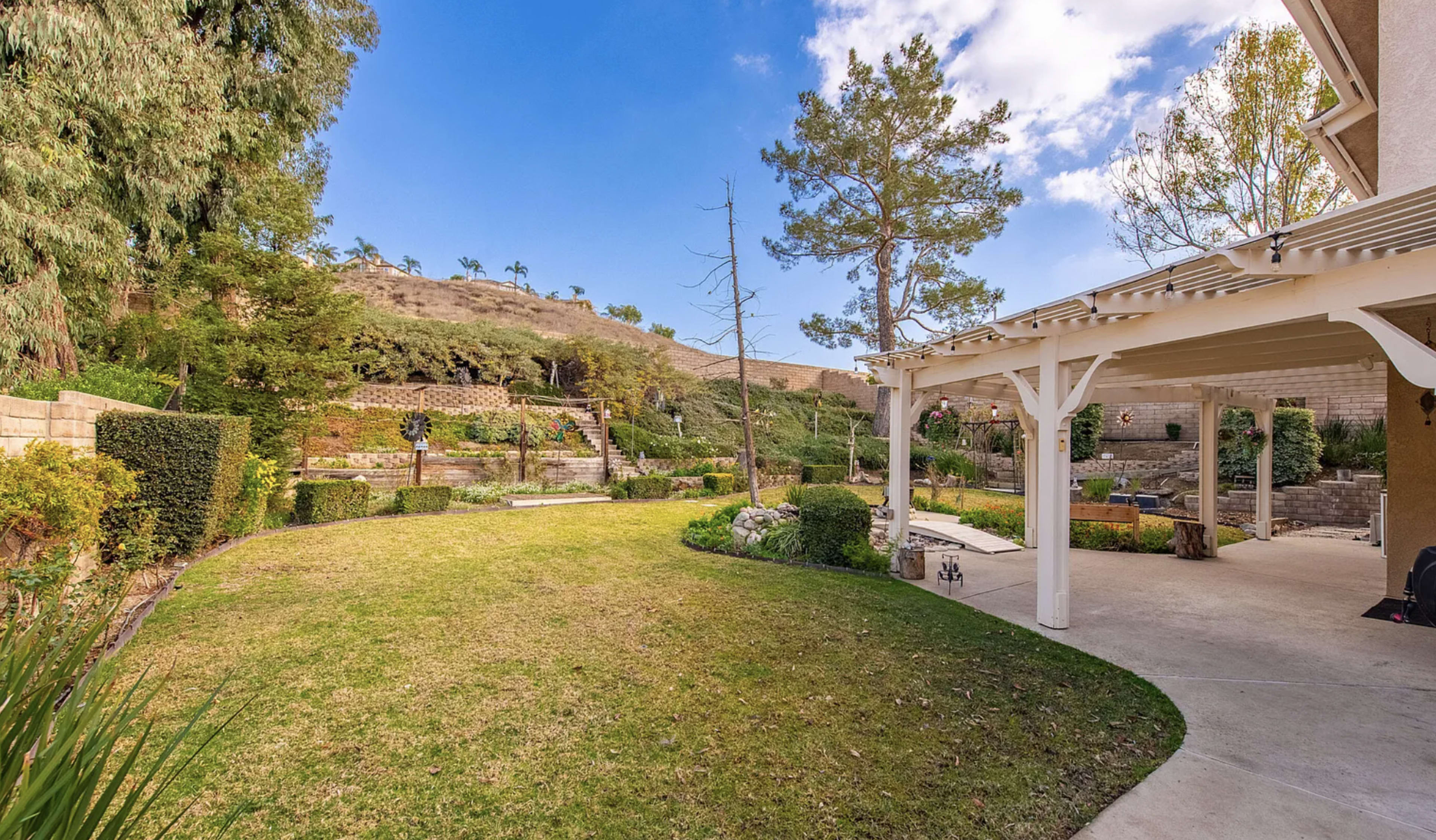 A landscaped backyard features neatly trimmed grass, shrubs, and stone steps leading up a hillside.