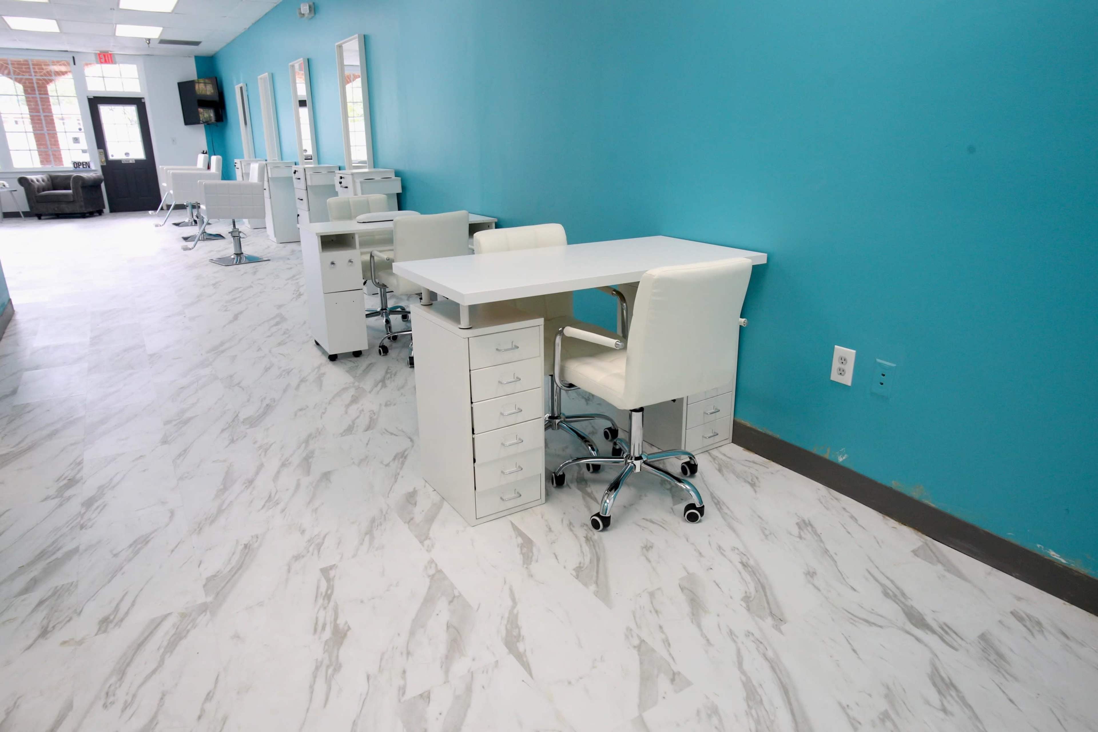 A brightly lit salon interior with white workstations and chairs against a turquoise wall.