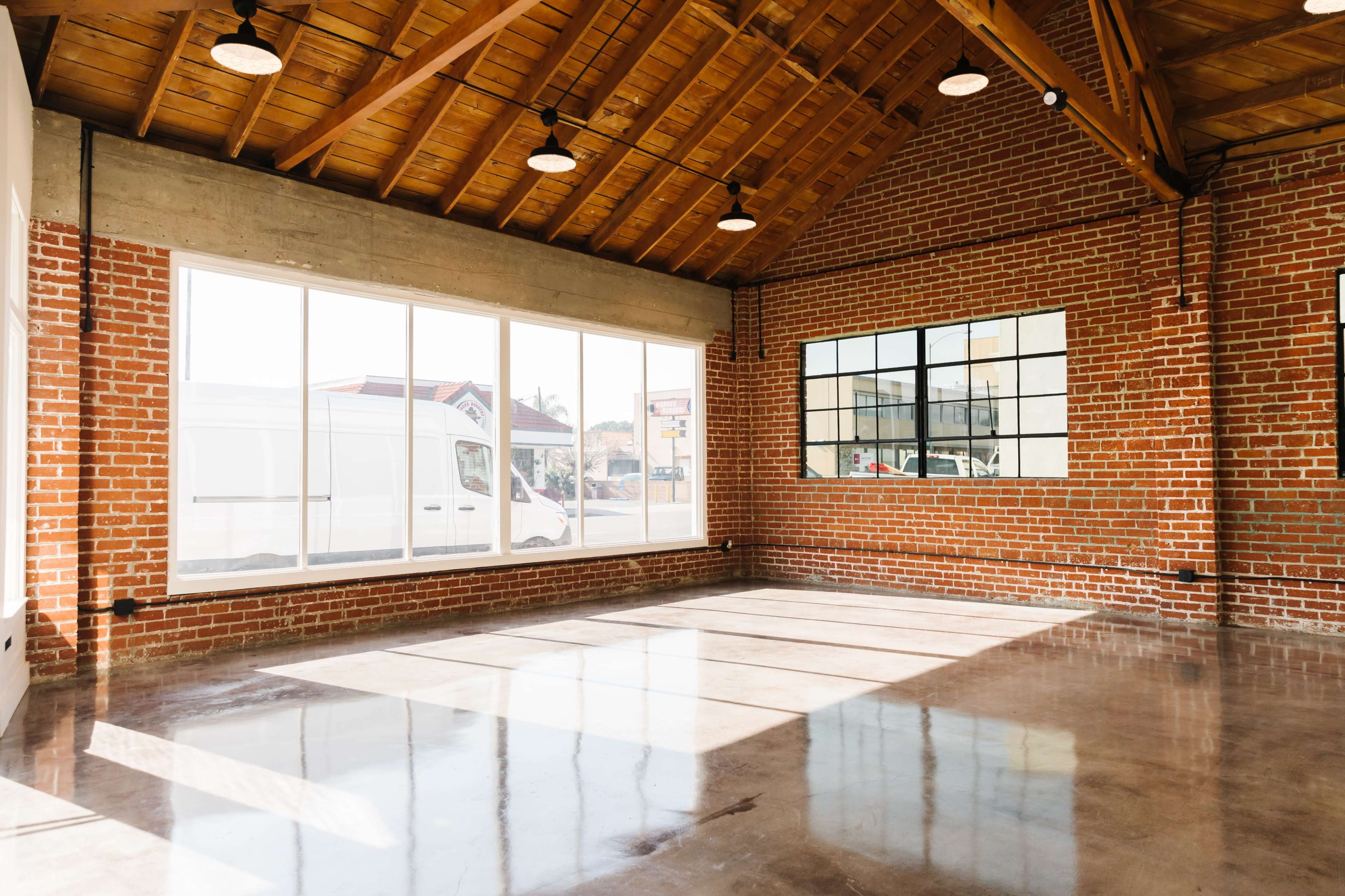 A spacious interior with brick walls, large windows, and polished concrete flooring, illuminated by overhead lights.