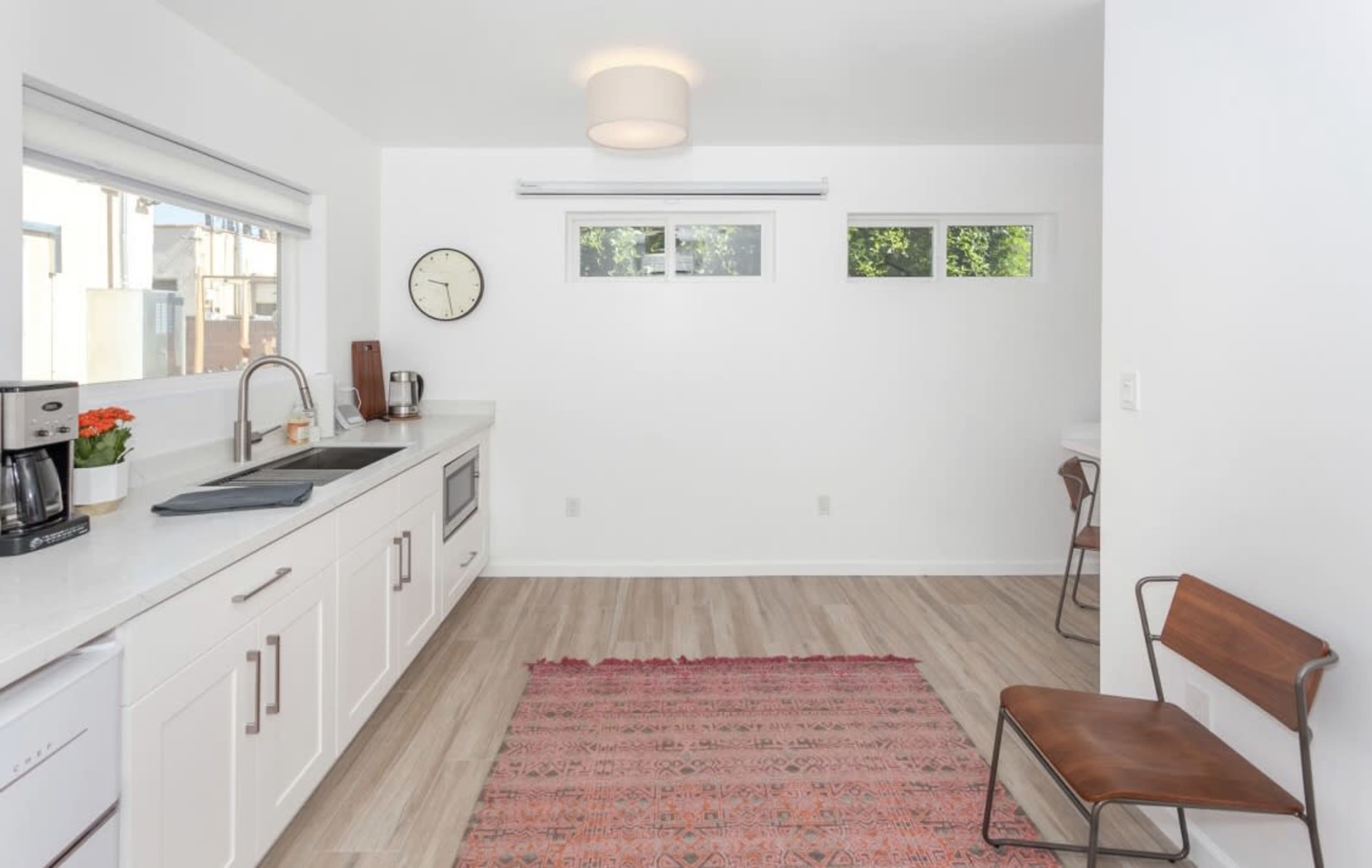 A modern kitchen with white cabinets, a stainless steel sink, and a small area rug on the wooden floor.