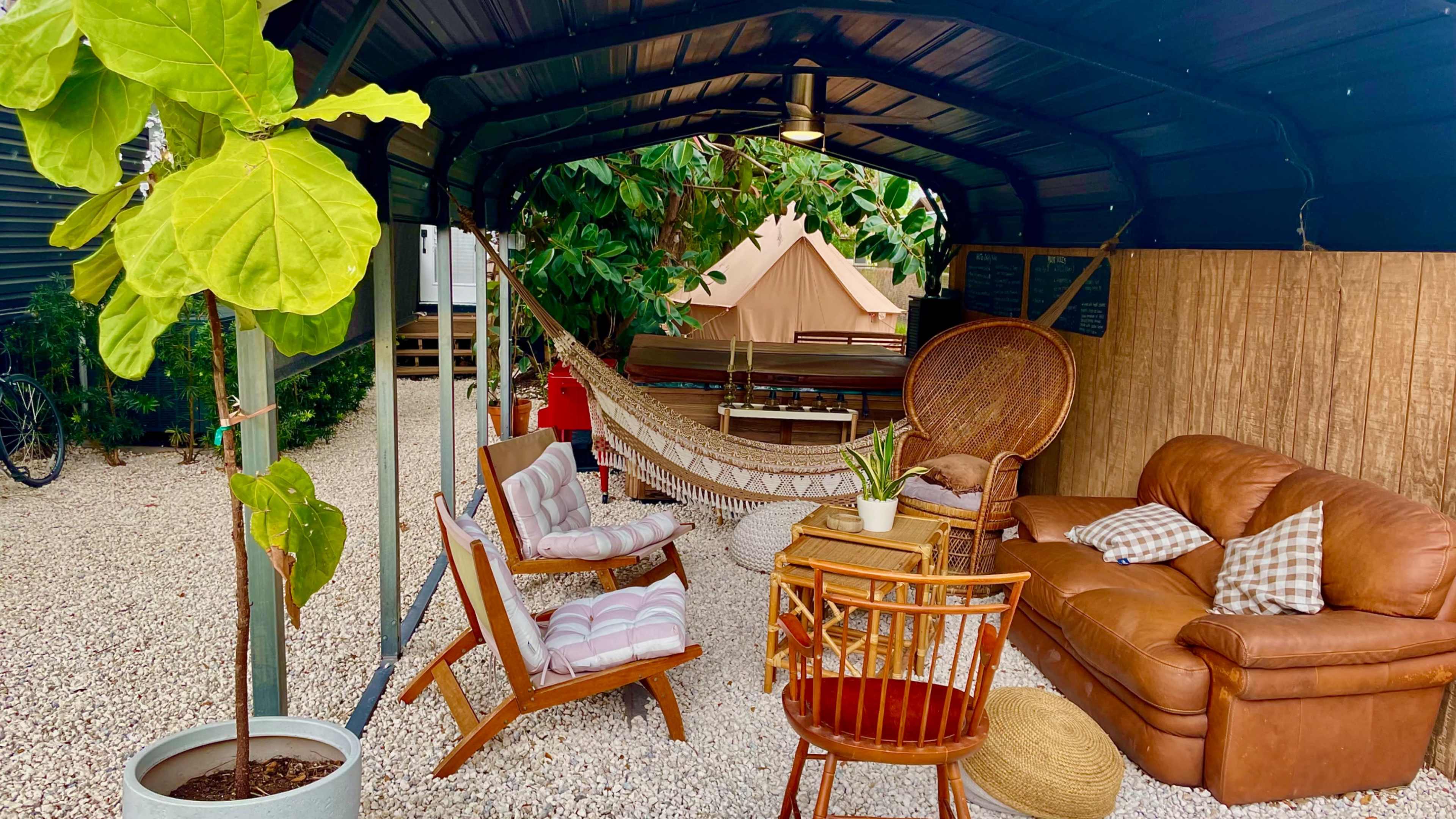A cozy outdoor seating area with a hammock, various chairs, and potted plants under a metal canopy.
