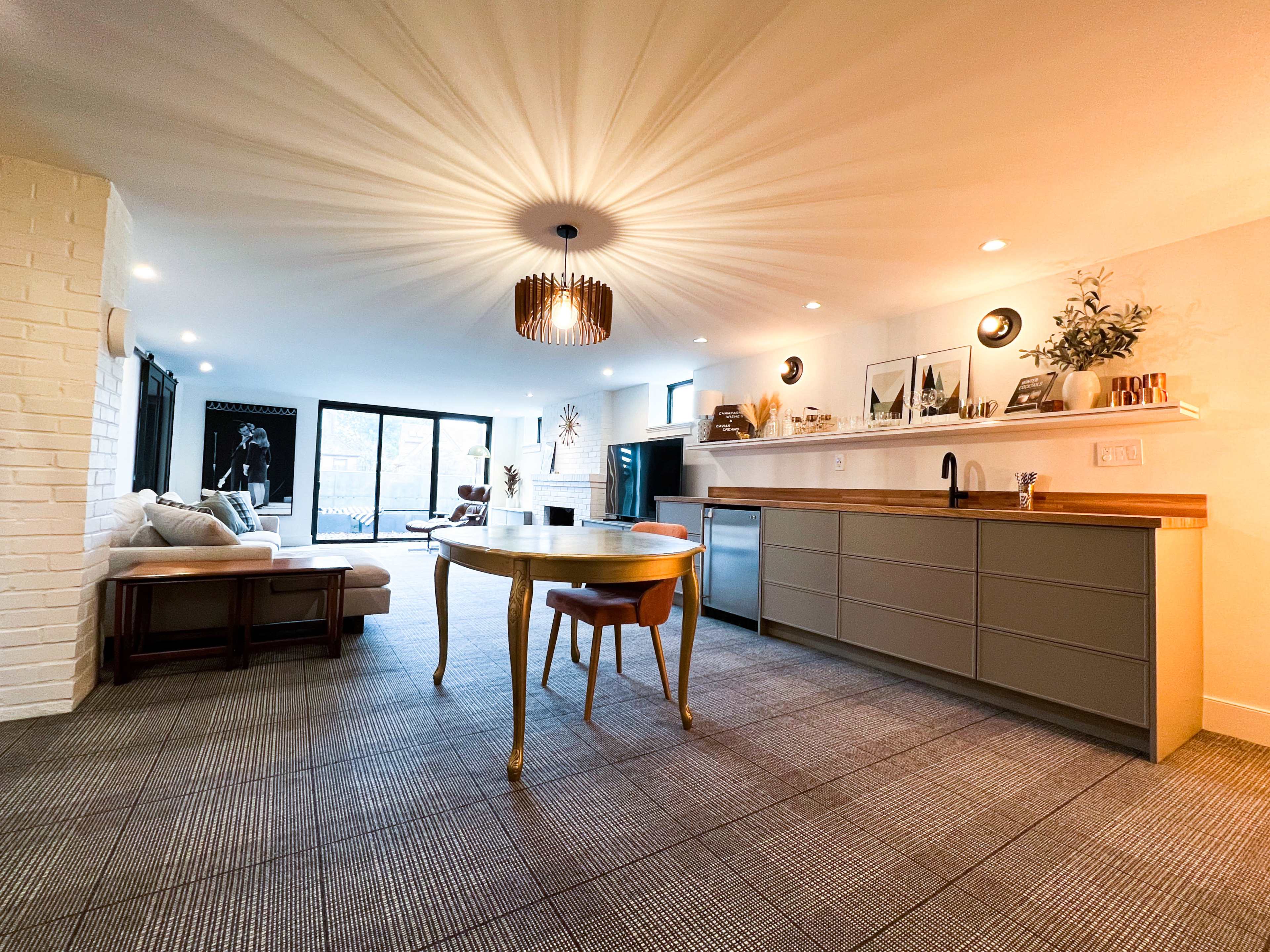 A modern living space with a circular dining table, a sofa area, and a kitchen section featuring a countertop and cabinets.