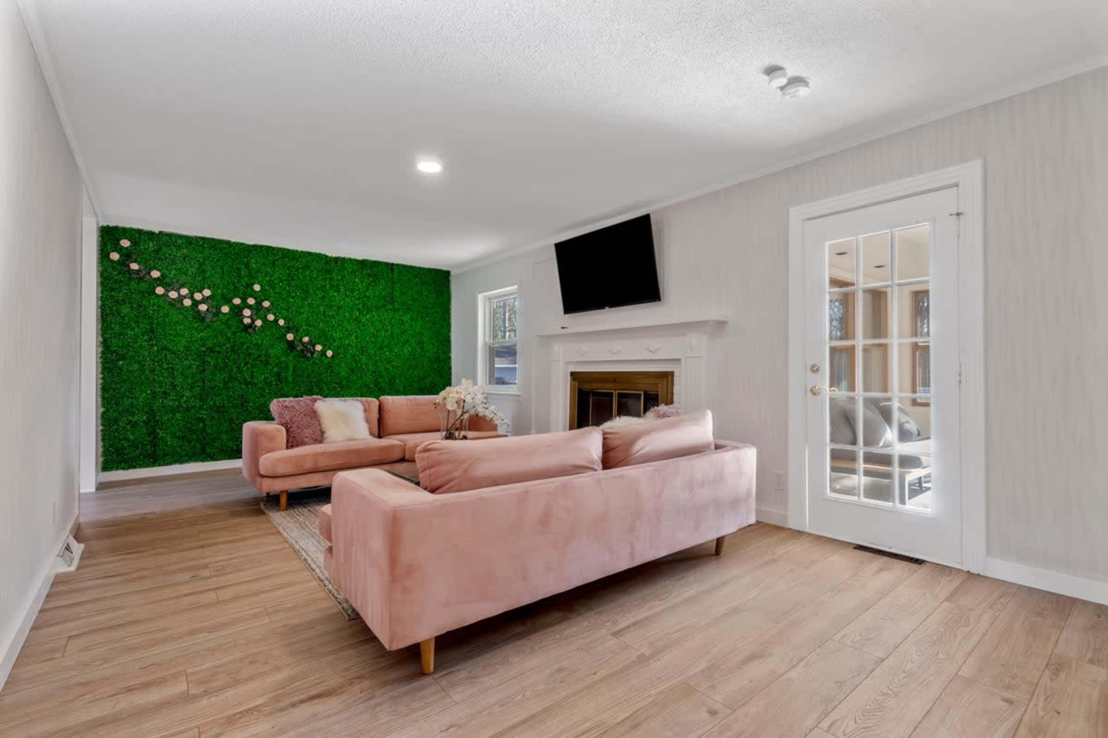 The living room features a pink sofa, a green moss wall, and a glass door leading to an outdoor space.