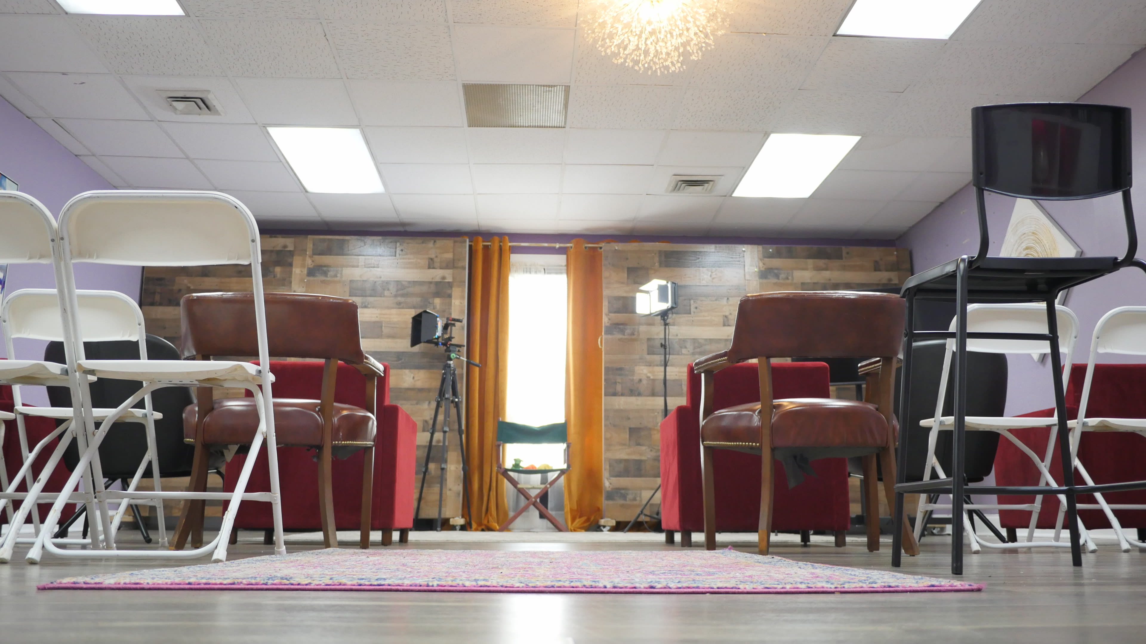 A room arranged with chairs facing a window, flanked by a pair of red armchairs and a rug on the floor.