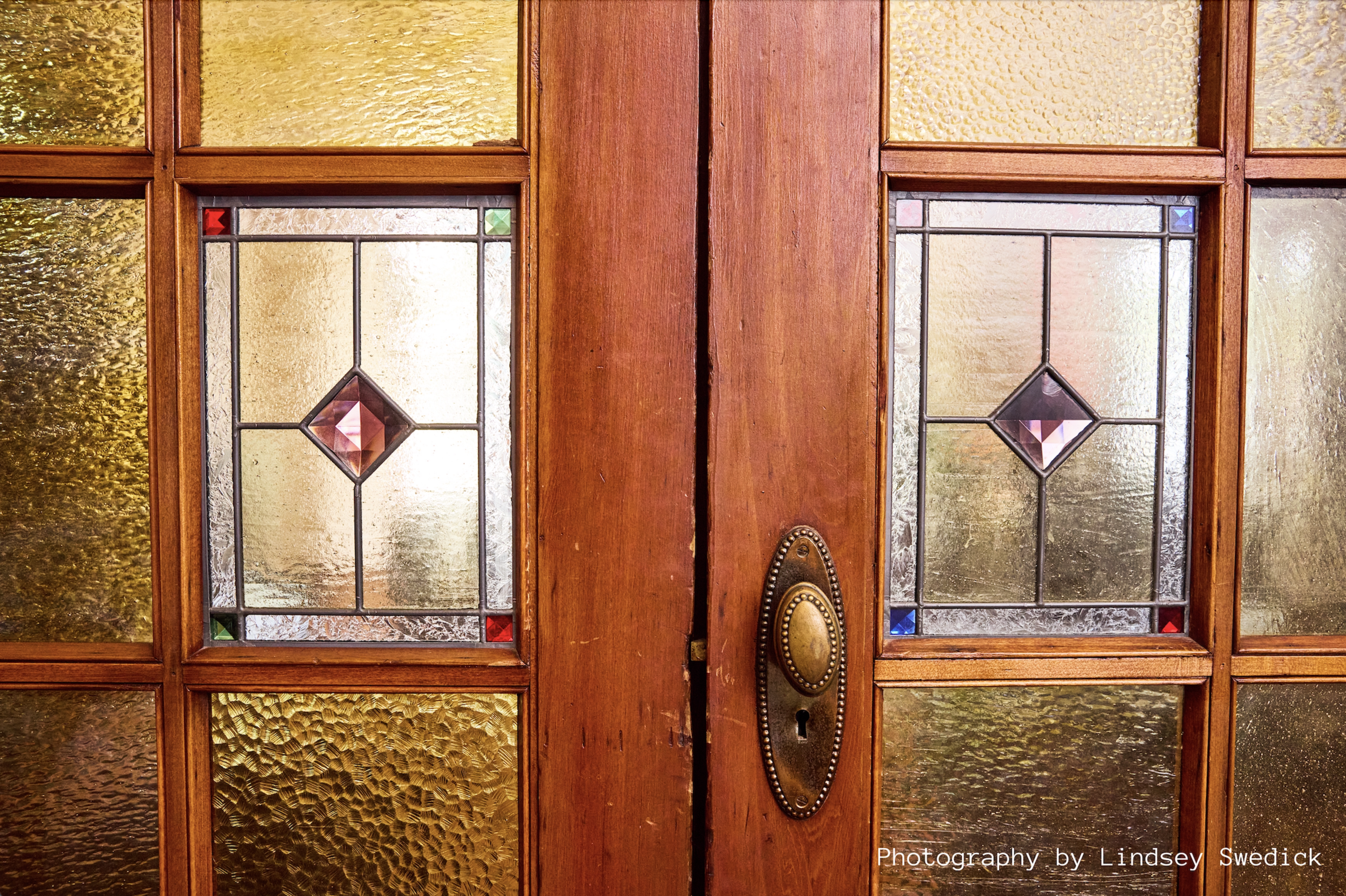 The image features a wooden door with decorative stained glass panels displaying geometric designs.