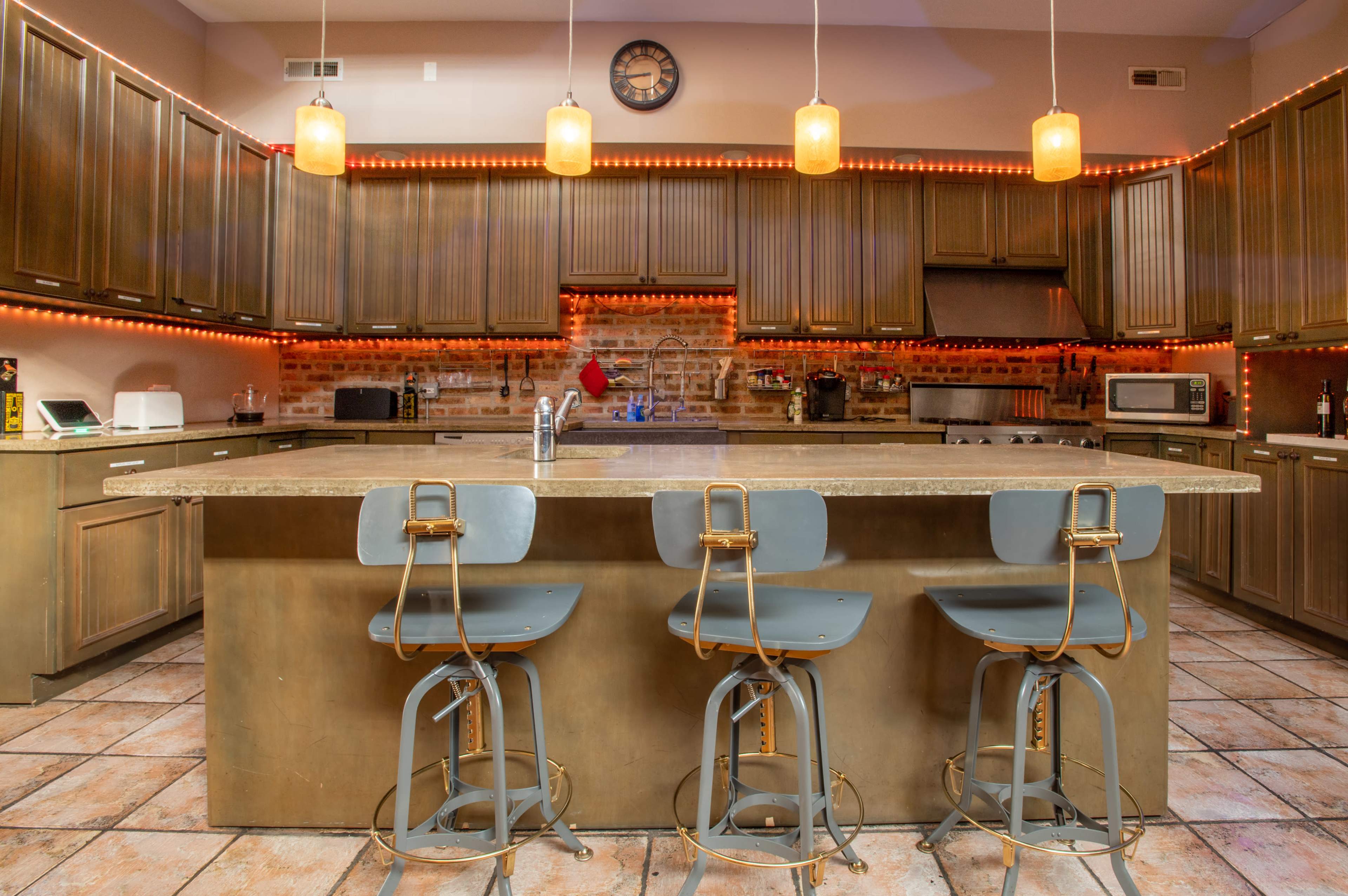 A modern kitchen features bronze cabinetry, a large central island with three metal stools, and ambient lighting along the countertops.