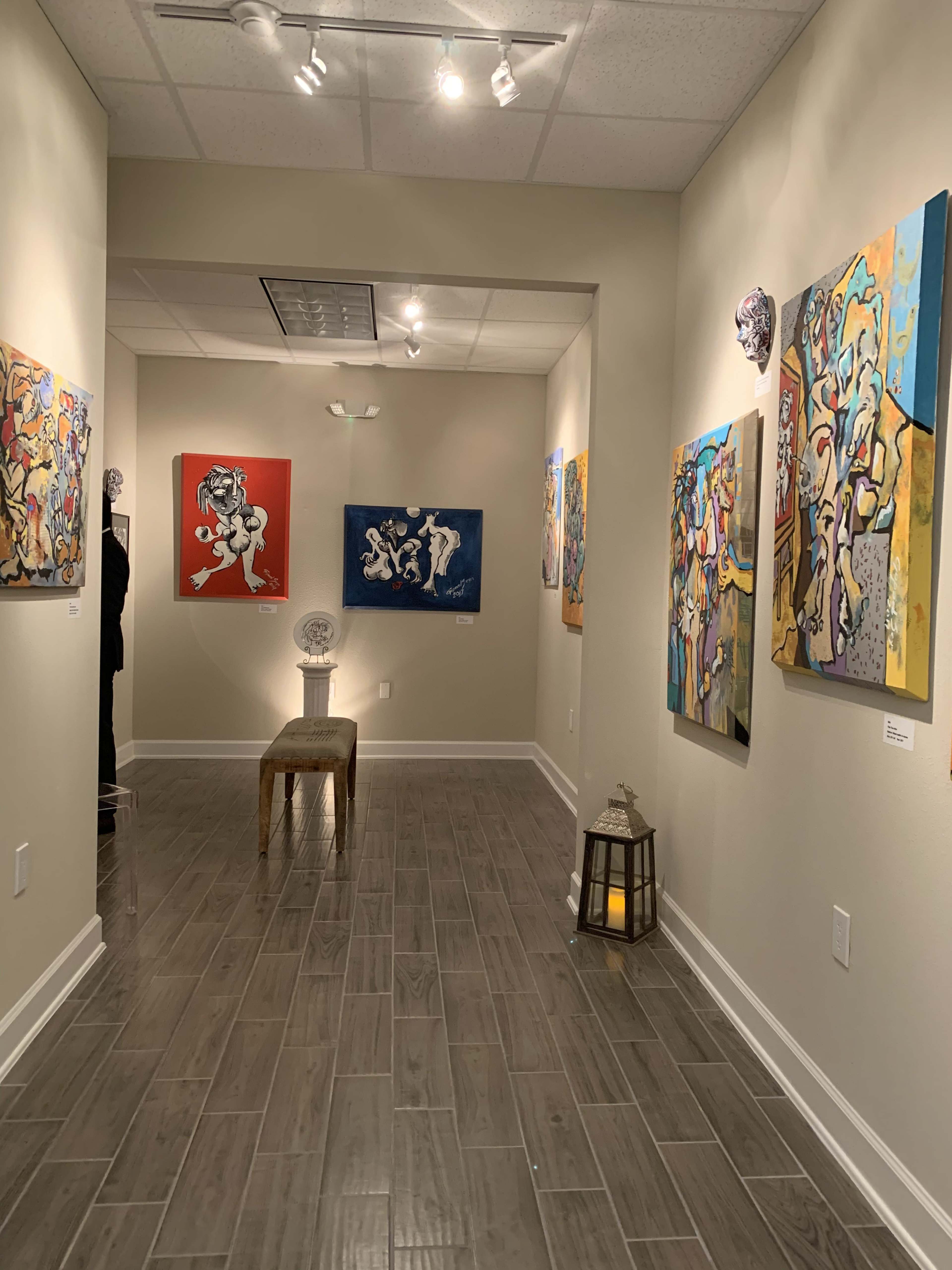 An art gallery corridor featuring colorful abstract paintings on the walls, a wooden stool in the center, and a lantern on the floor.