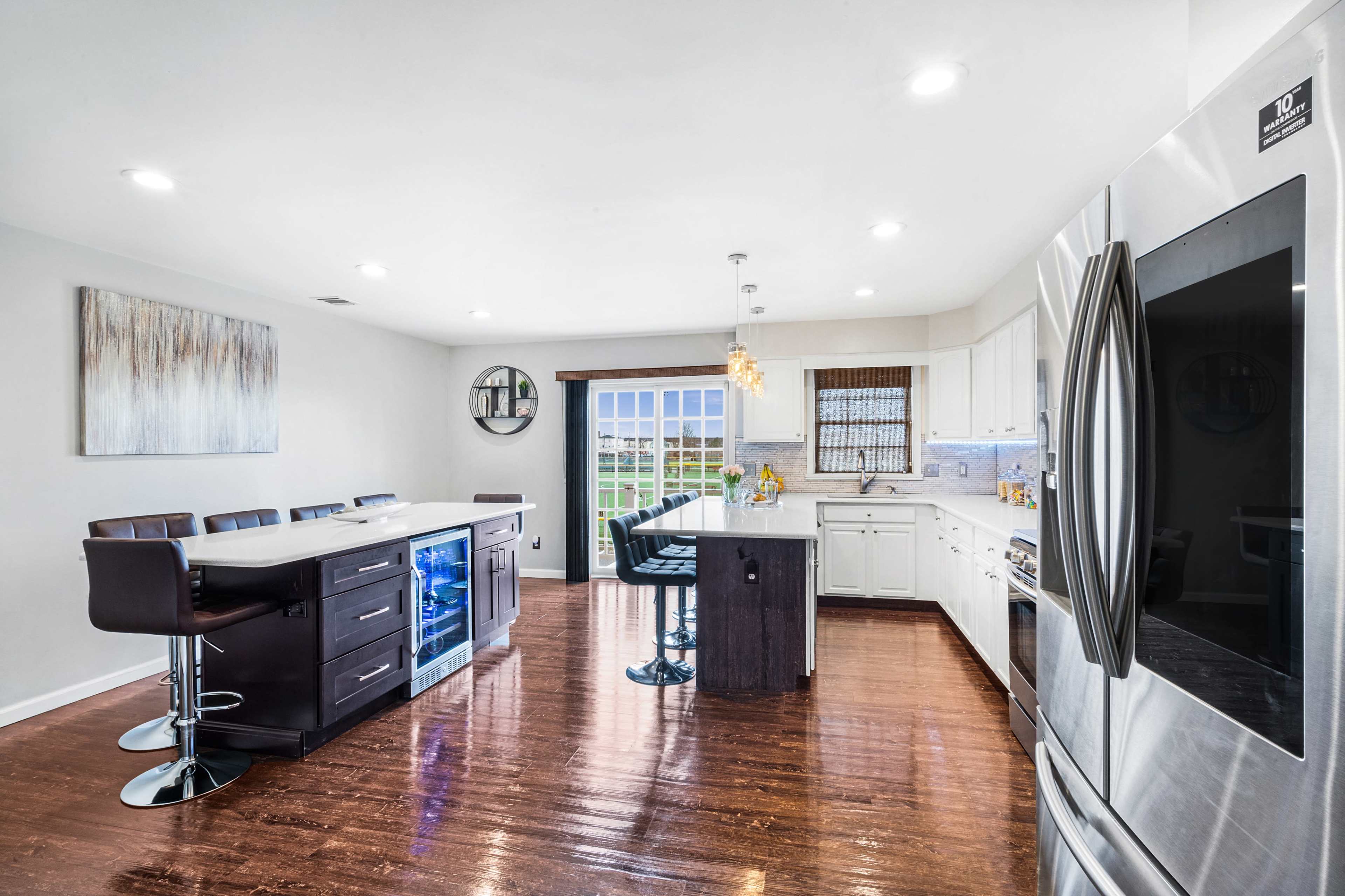 A modern kitchen features stainless steel appliances, a central island with seating, and large windows overlooking a landscaped exterior.