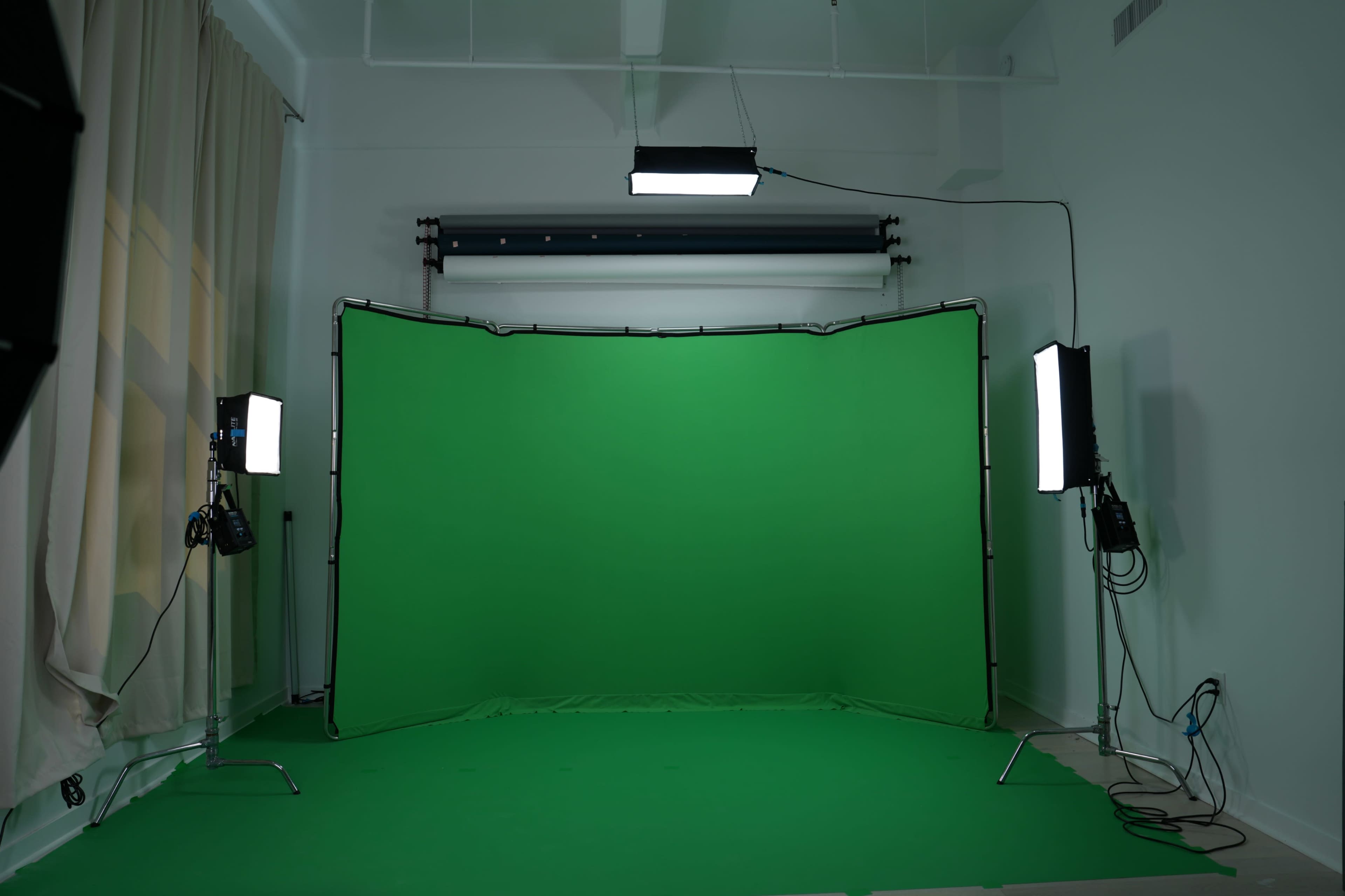 The image shows a photography studio featuring a large green backdrop, with softbox lights on either side, and a minimalistic white interior.