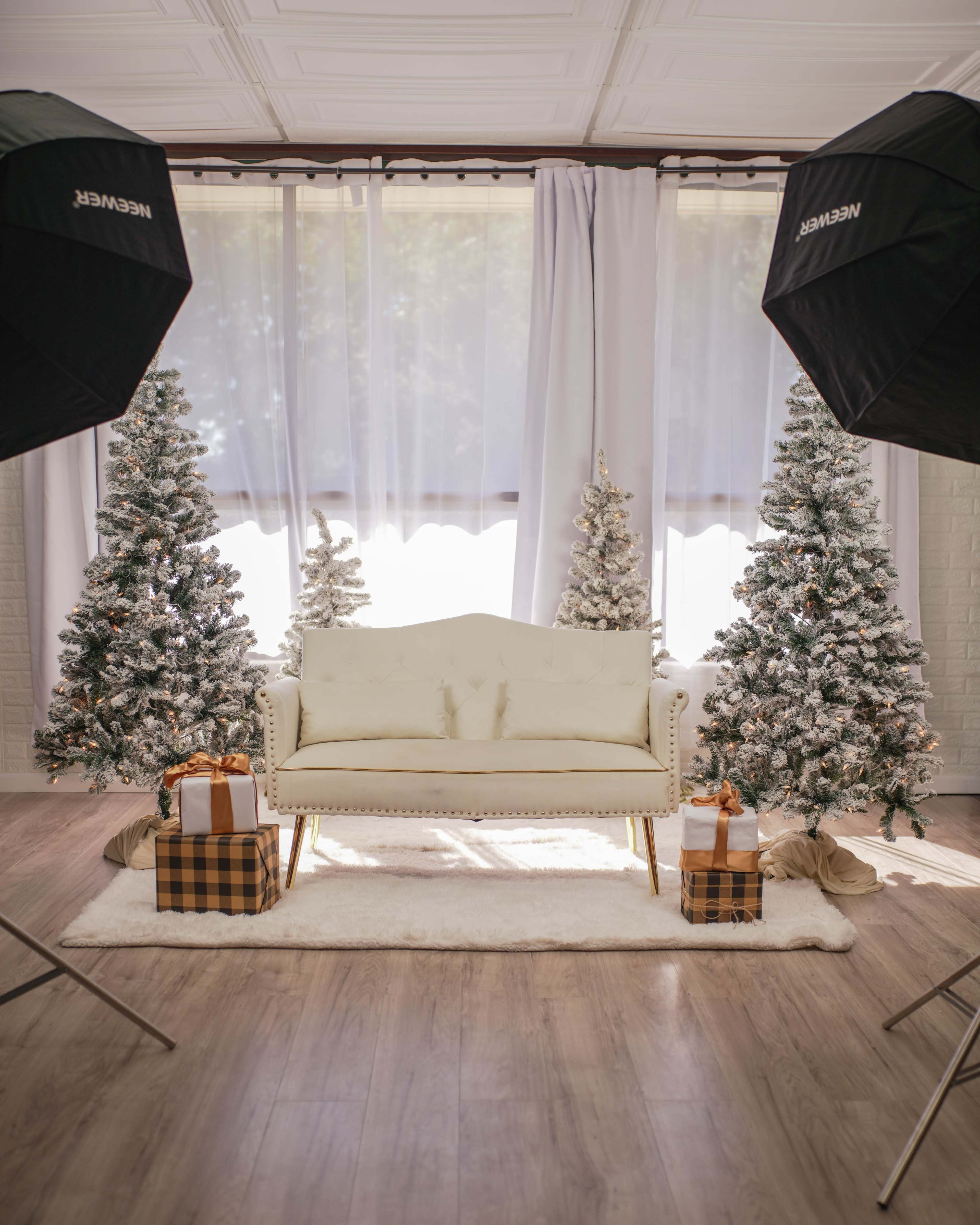 The image features a cozy holiday-themed room with a white couch centered between two snow-dusted Christmas trees, surrounded by wrapped gifts on a plush rug.