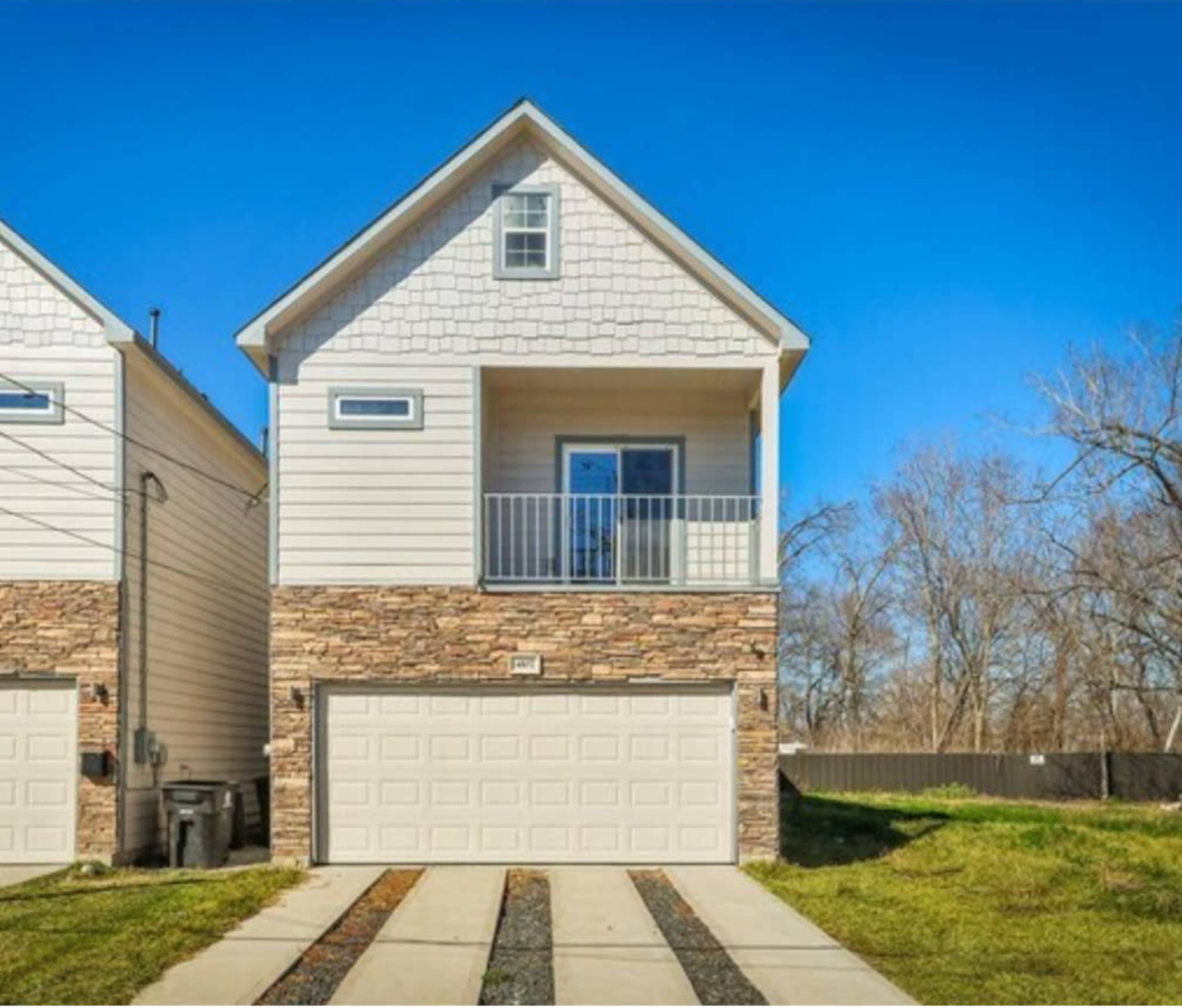 The image shows a two-story house with a stone-accented facade, a front balcony, and a two-car garage.